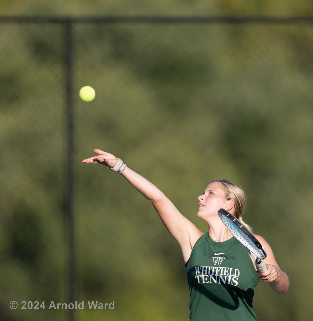 Tennis player serves the ball during a match on outdoor court.