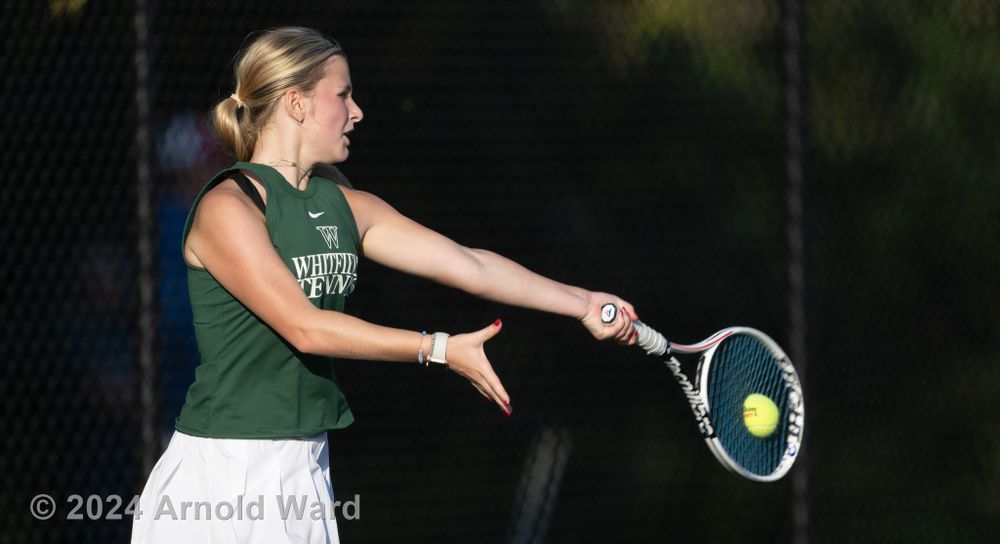 Tennis player hits a forehand return during match on outdoor court.