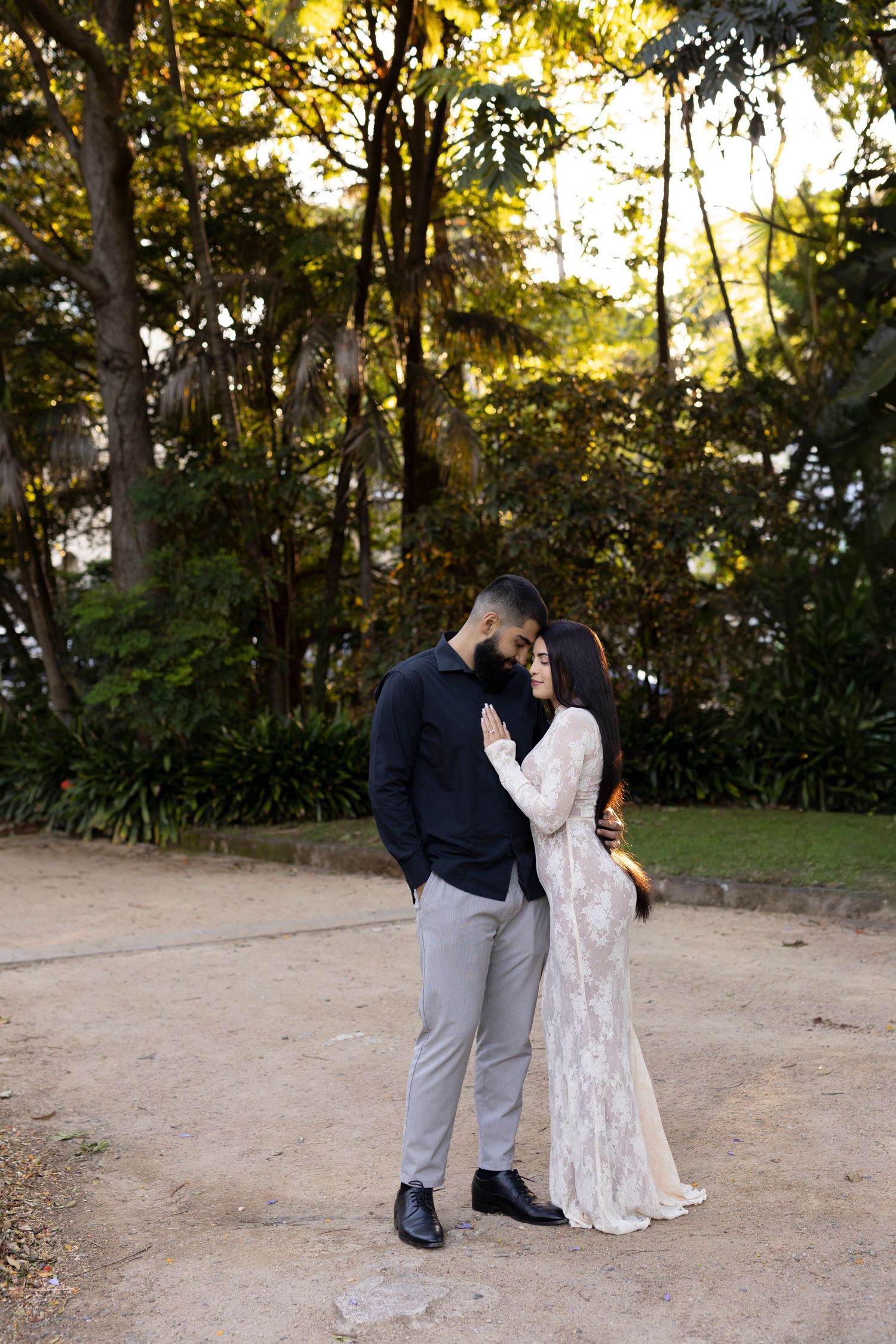 Couple in elegant attire sharing a romantic moment in a lush green park during golden hour.