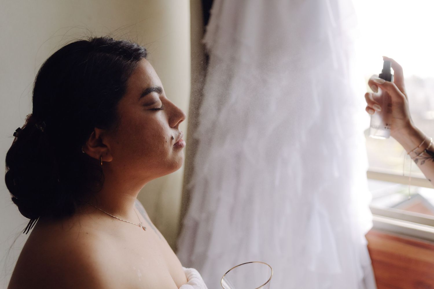 Bride with updo hairstyle gets makeup setting spray applied before her wedding ceremony.