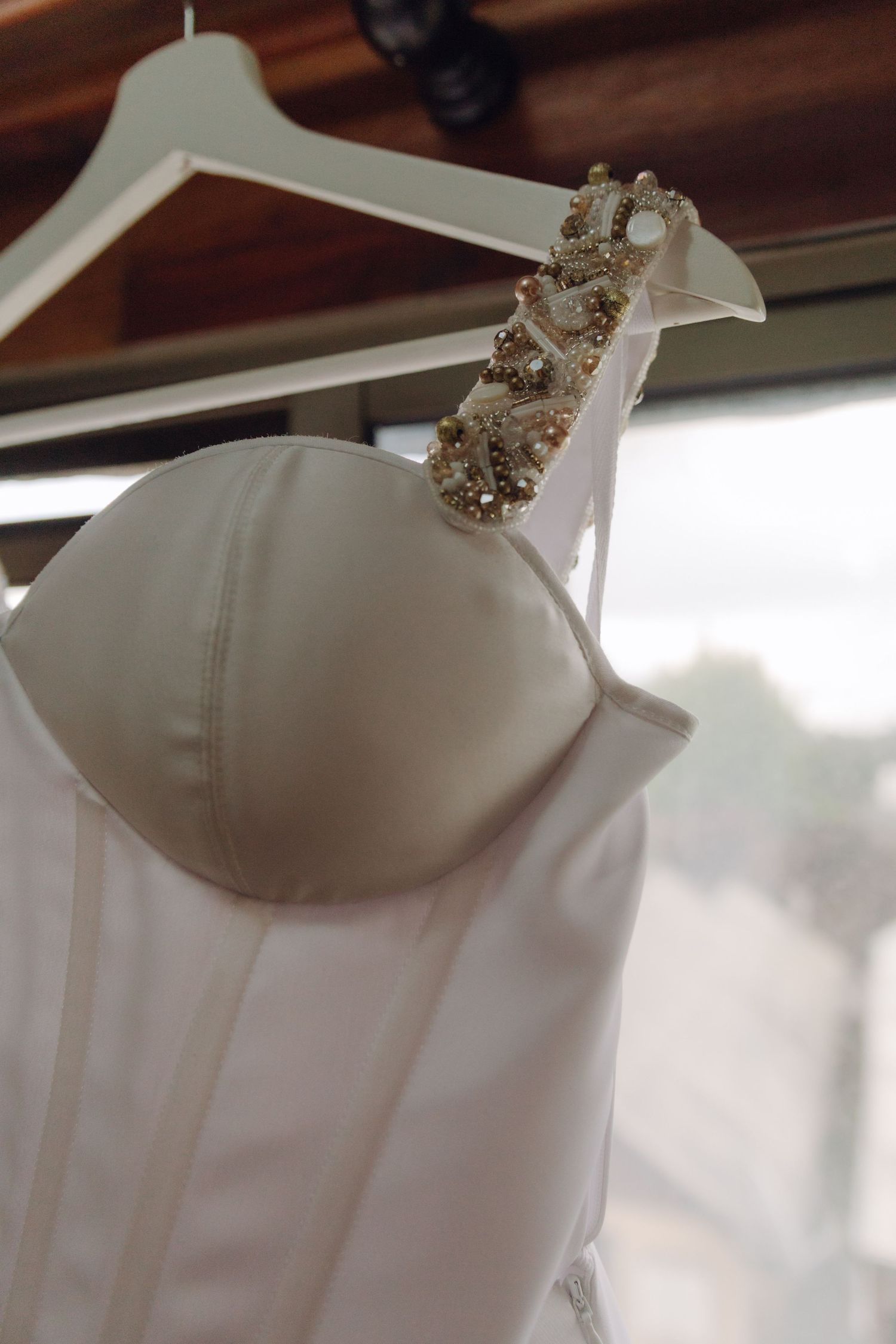 Close-up detail of white wedding dress bodice with ornate gold and pearl embellished strap.