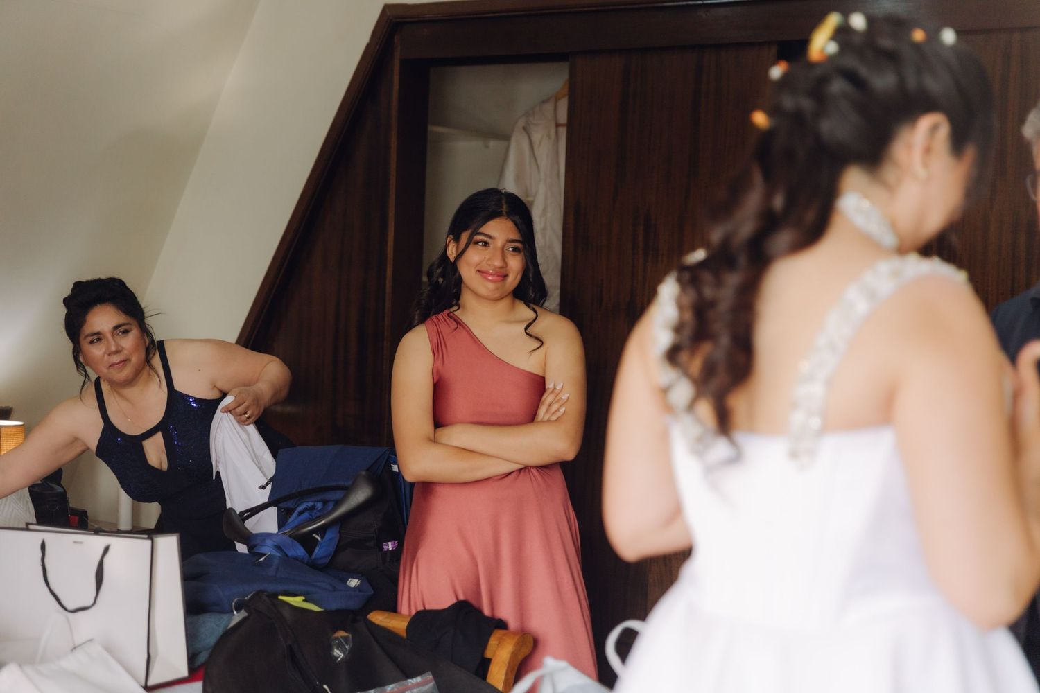 Bridesmaids in colorful dresses watching the bride in her white wedding gown during bridal prep.