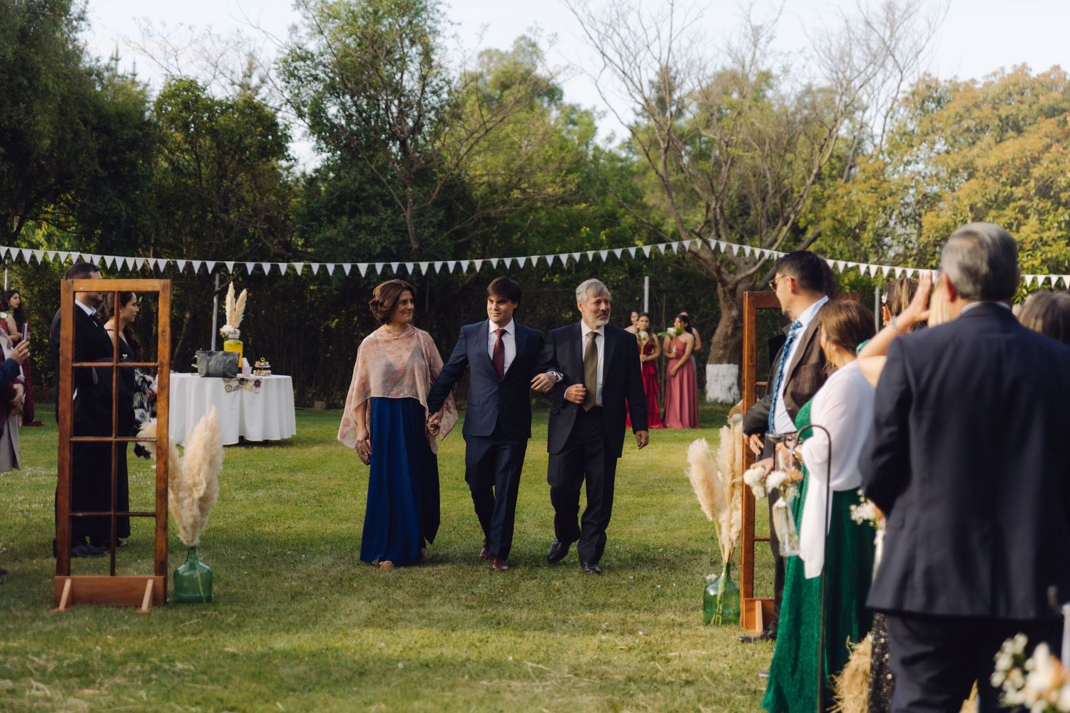 Wedding party walking down the outdoor aisle at a garden ceremony decorated with bunting flags.