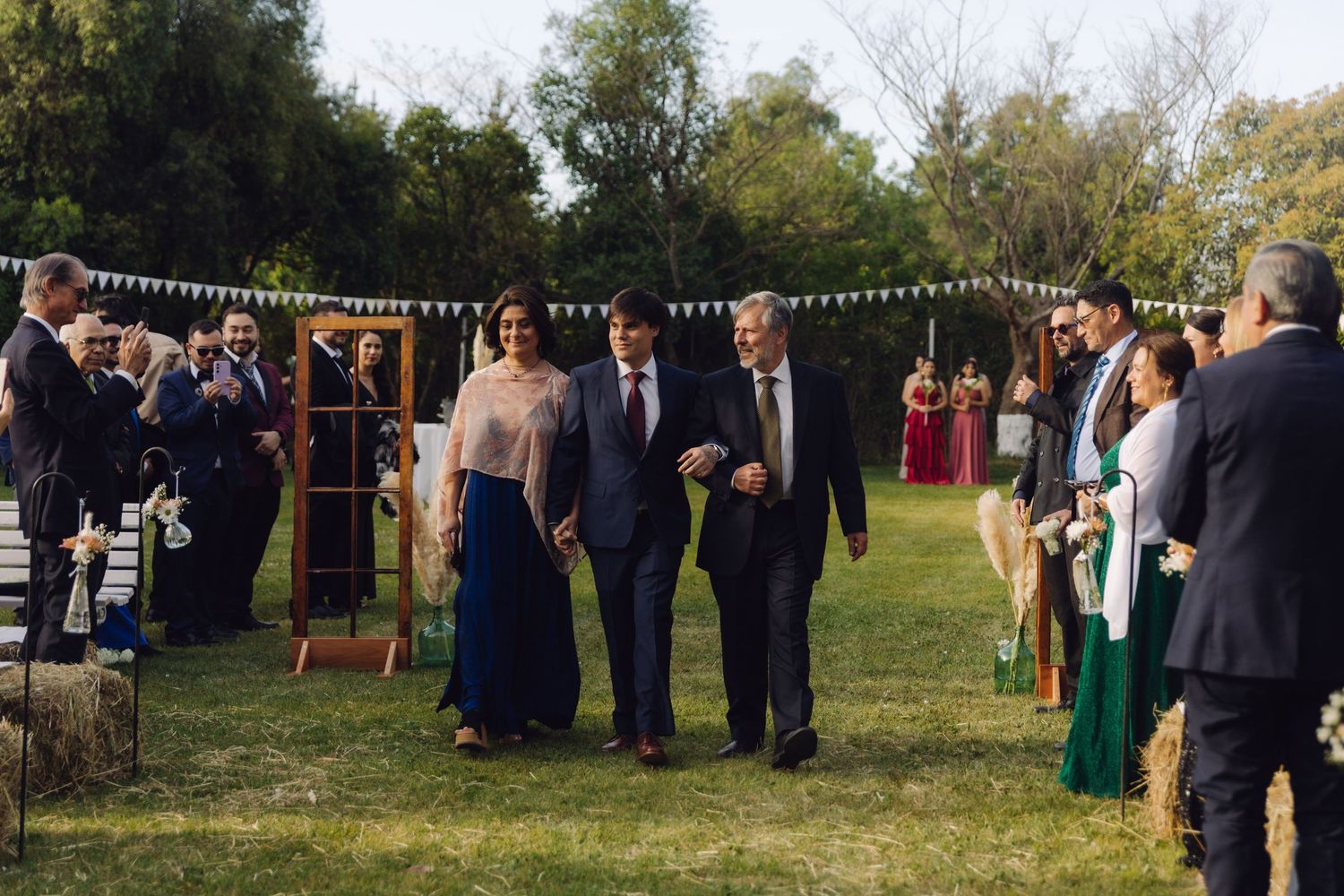 Couple escorted by family members walking down a grass aisle at an outdoor wedding ceremony.