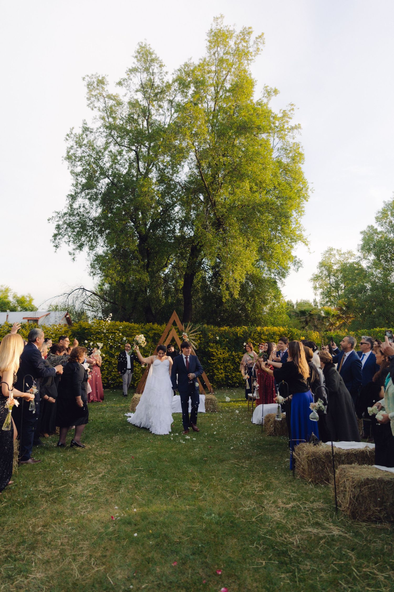 Newlyweds walk down the aisle as guests celebrate at an outdoor garden wedding ceremony.
