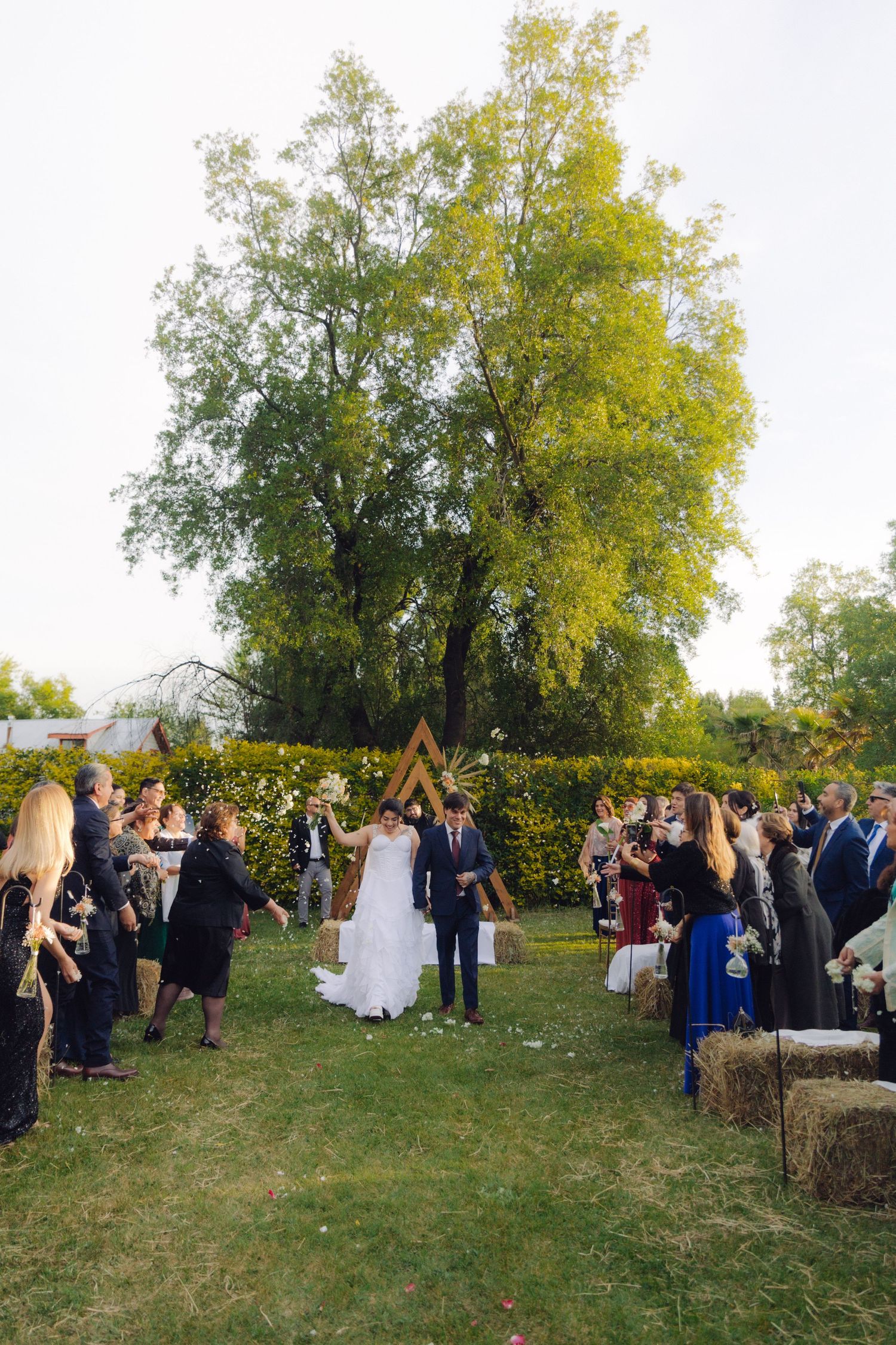 Bride and groom exit ceremony as guests cheer along the aisle at an outdoor garden wedding.