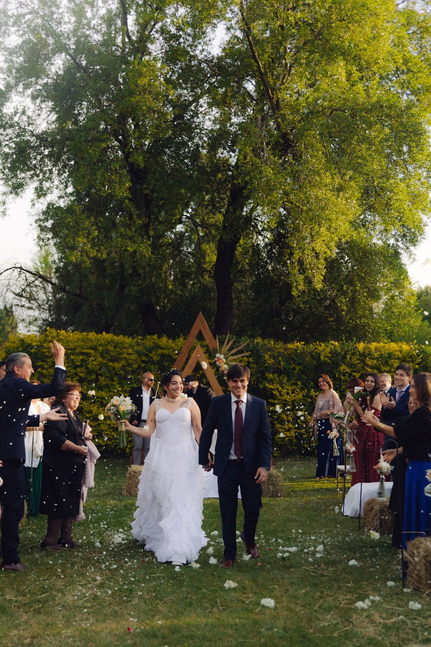 Smiling bride and groom walk through confetti at their outdoor garden wedding recessional.