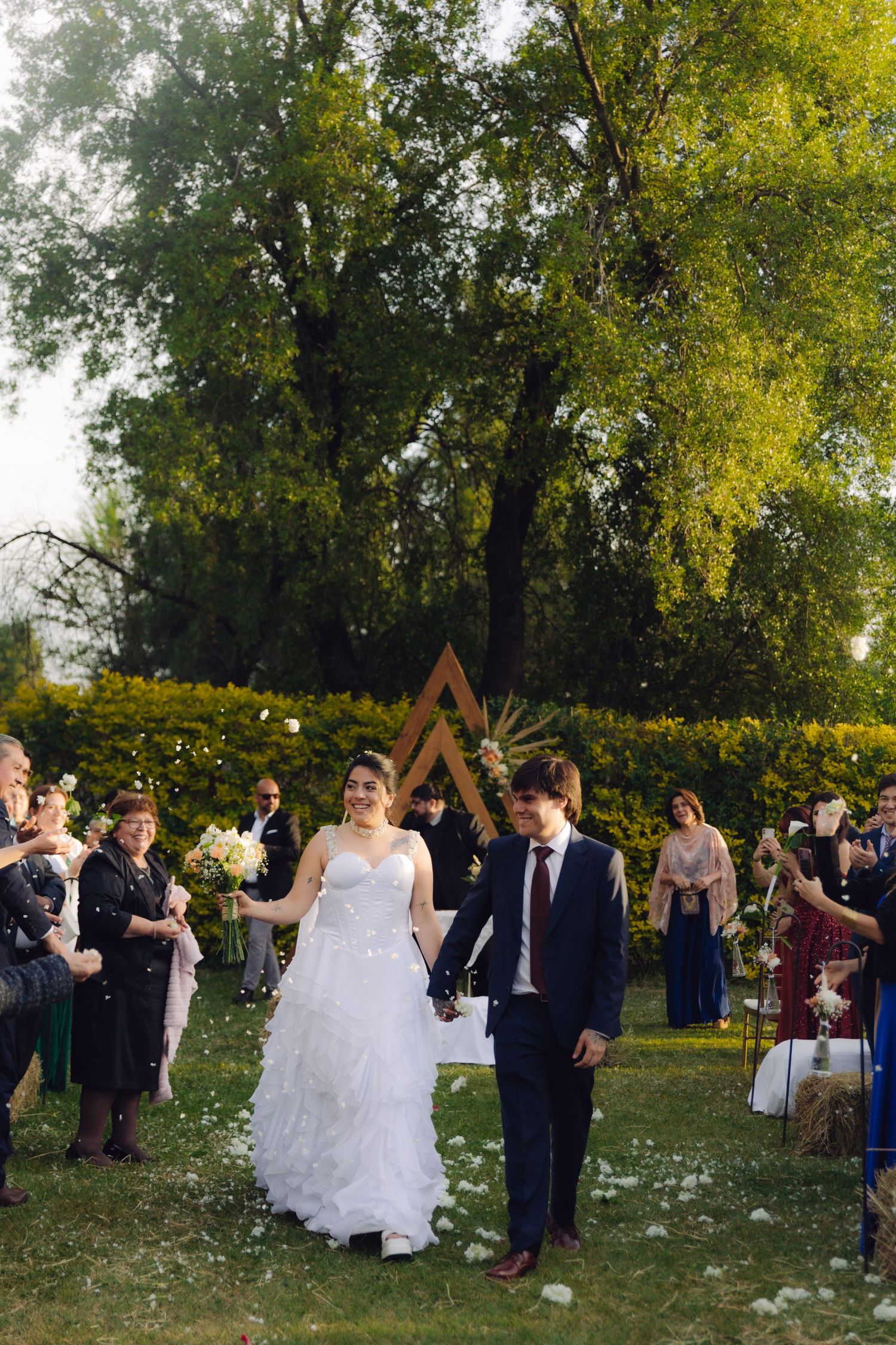 Bride and groom walk hand in hand through confetti during outdoor garden wedding recessional.