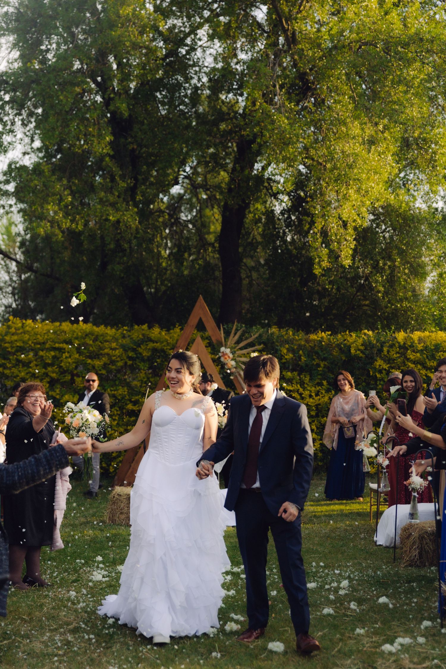 Bride and groom walk down outdoor aisle as guests celebrate their wedding ceremony in a lush garden.