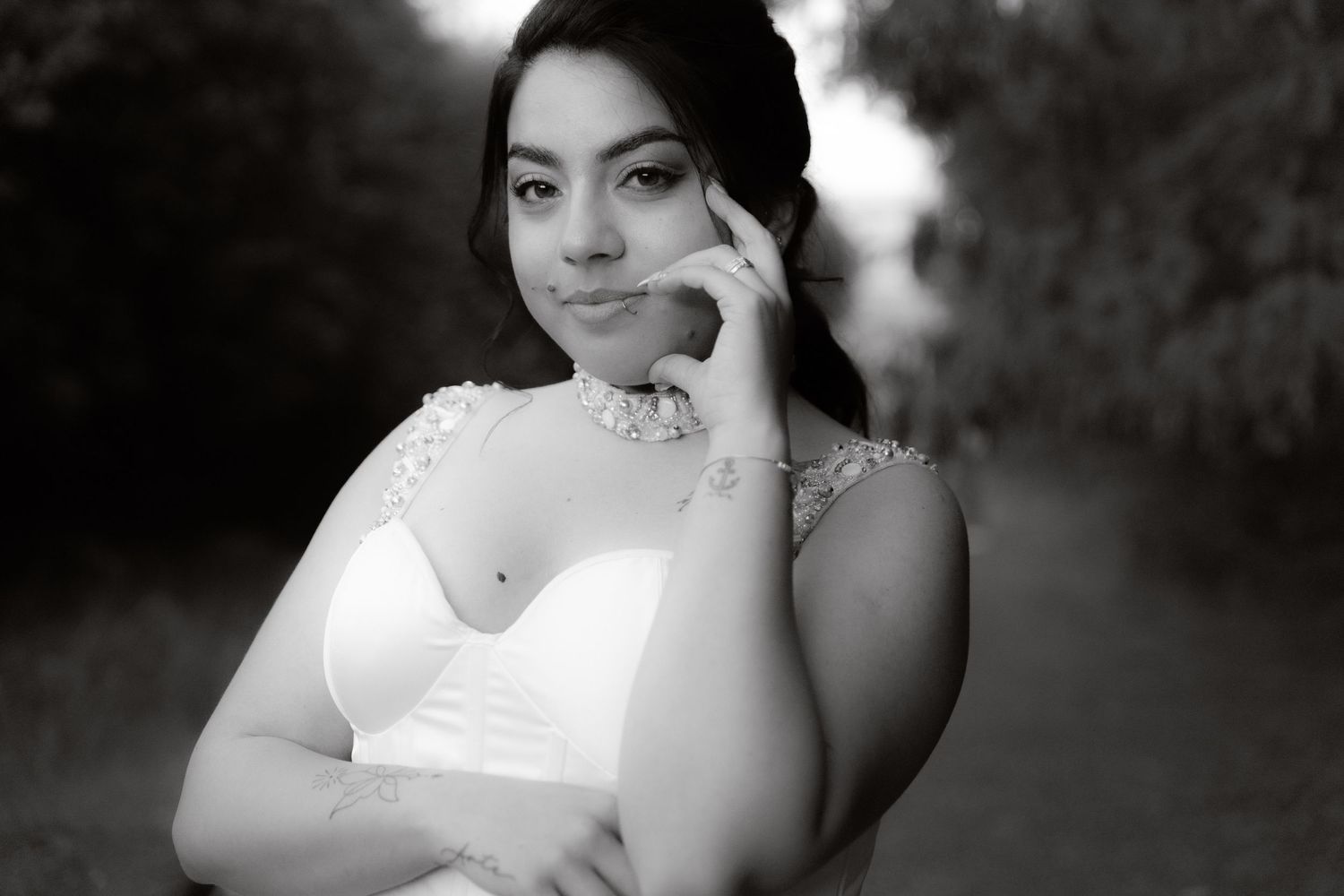 Black and white close-up portrait of a smiling bride in white gown along a softly blurred garden path.