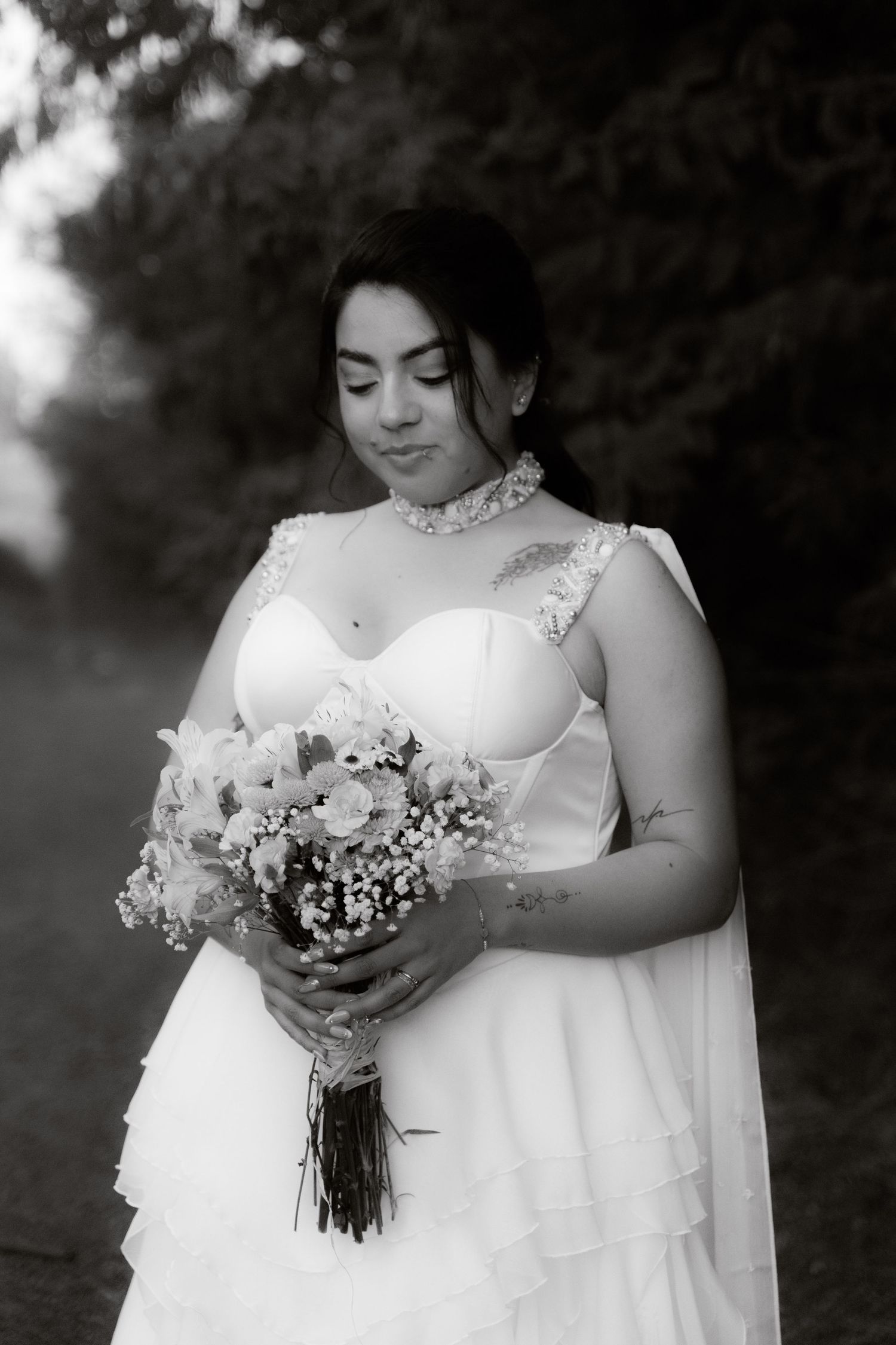 Black and white portrait of a bride in a white gown holding a floral bouquet in a garden setting.