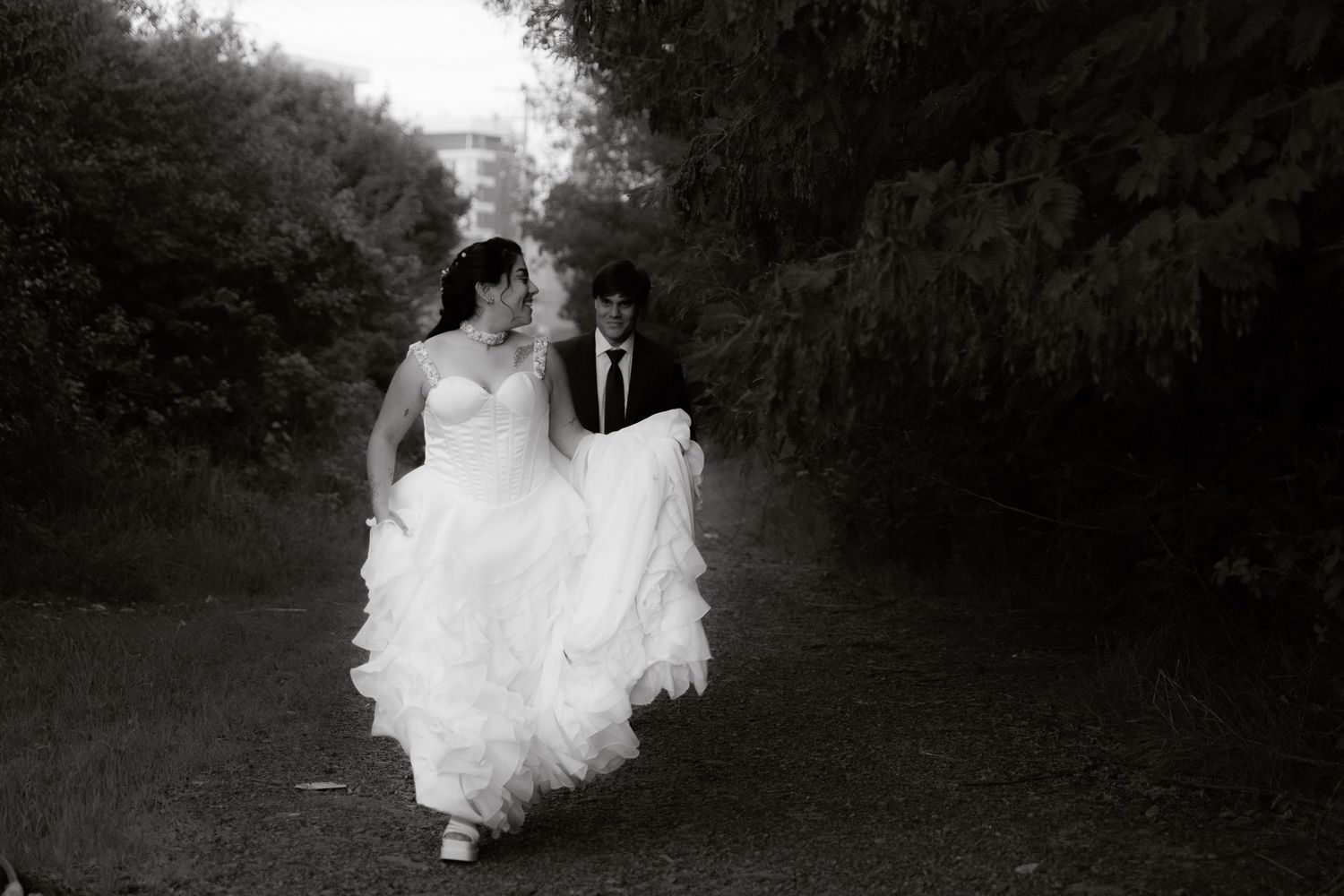 Black and white candid photo of a bride and groom walking joyfully along a garden pathway.