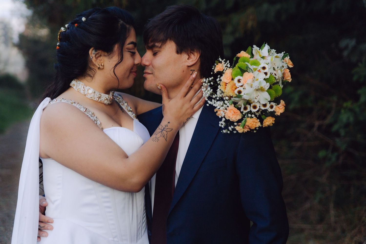 Wedding couple nearly kissing, bride in white gown with jeweled neckline holding floral bouquet.