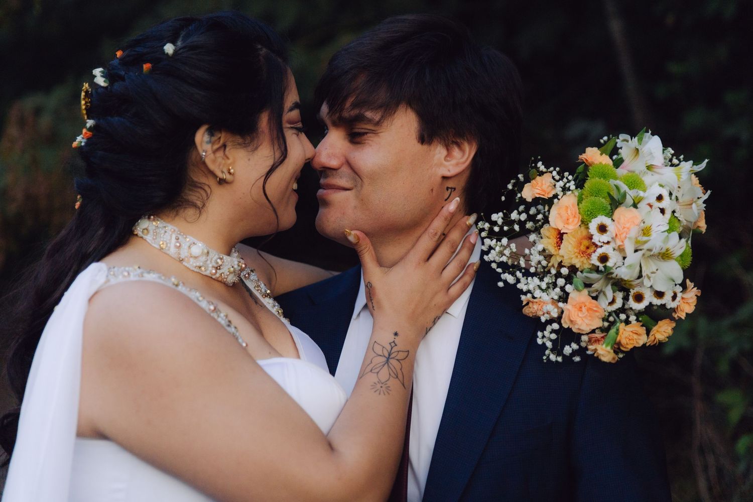 Bride and groom sharing a tender almost-kiss, bride holding peach and white bouquet outdoors.