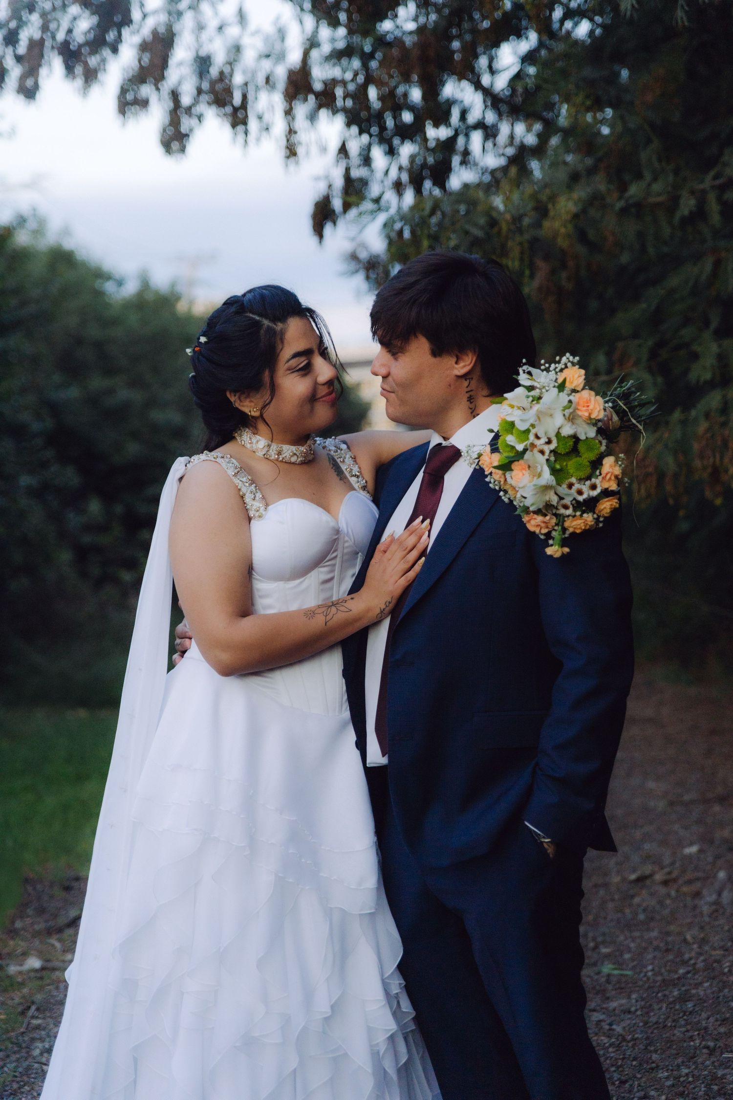 Bride in ruffled white gown and groom in navy suit gazing at each other in garden setting.