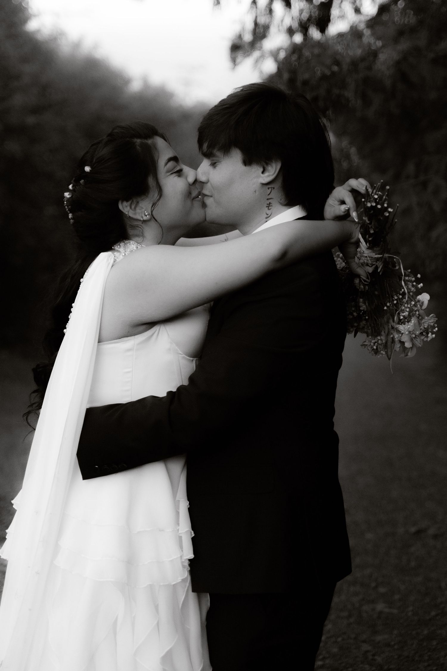 Black and white photo of bride and groom kissing while embracing outdoors on their wedding day.