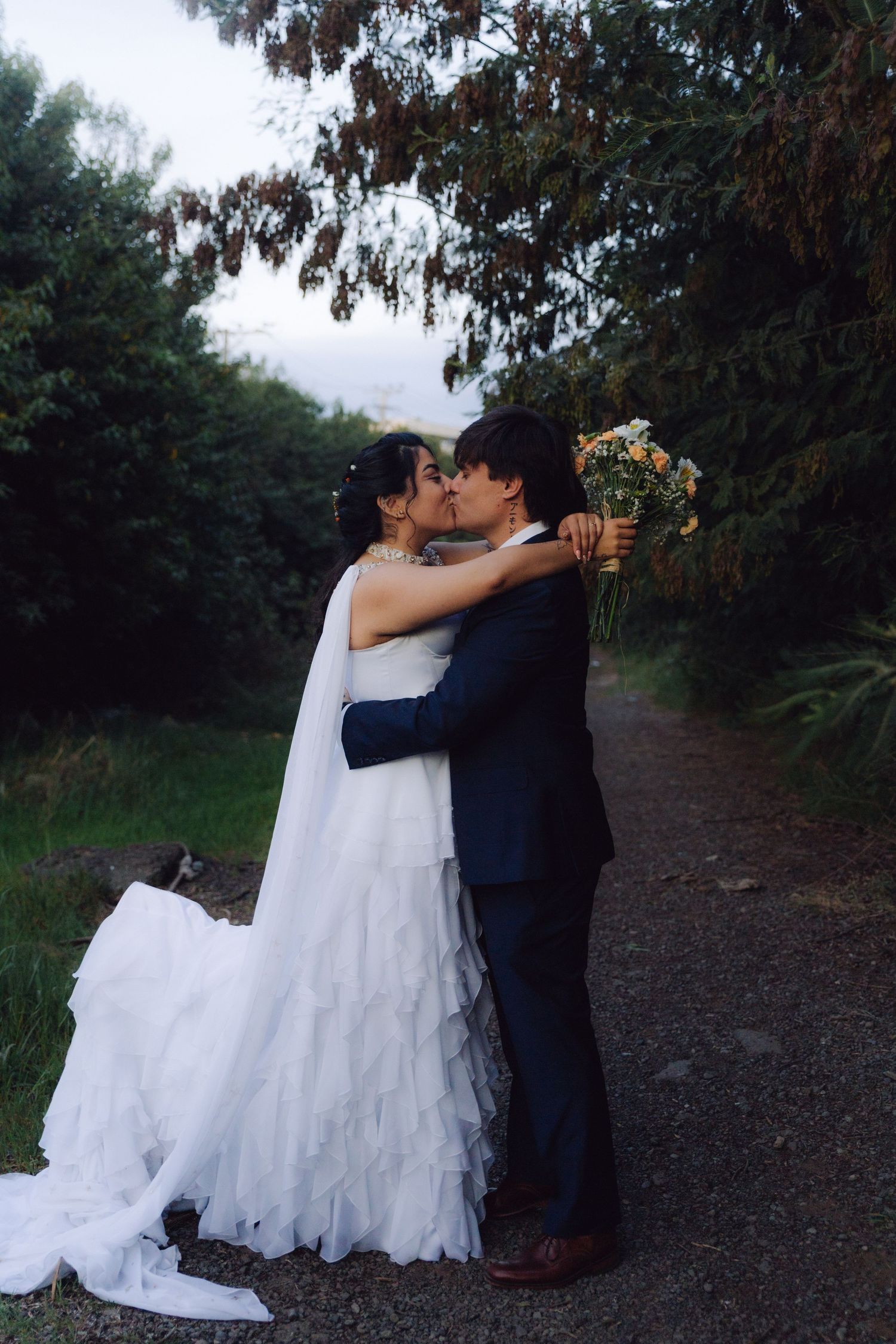 Wedding couple kissing on a garden path, bride in ruffled white gown holding colorful bouquet.