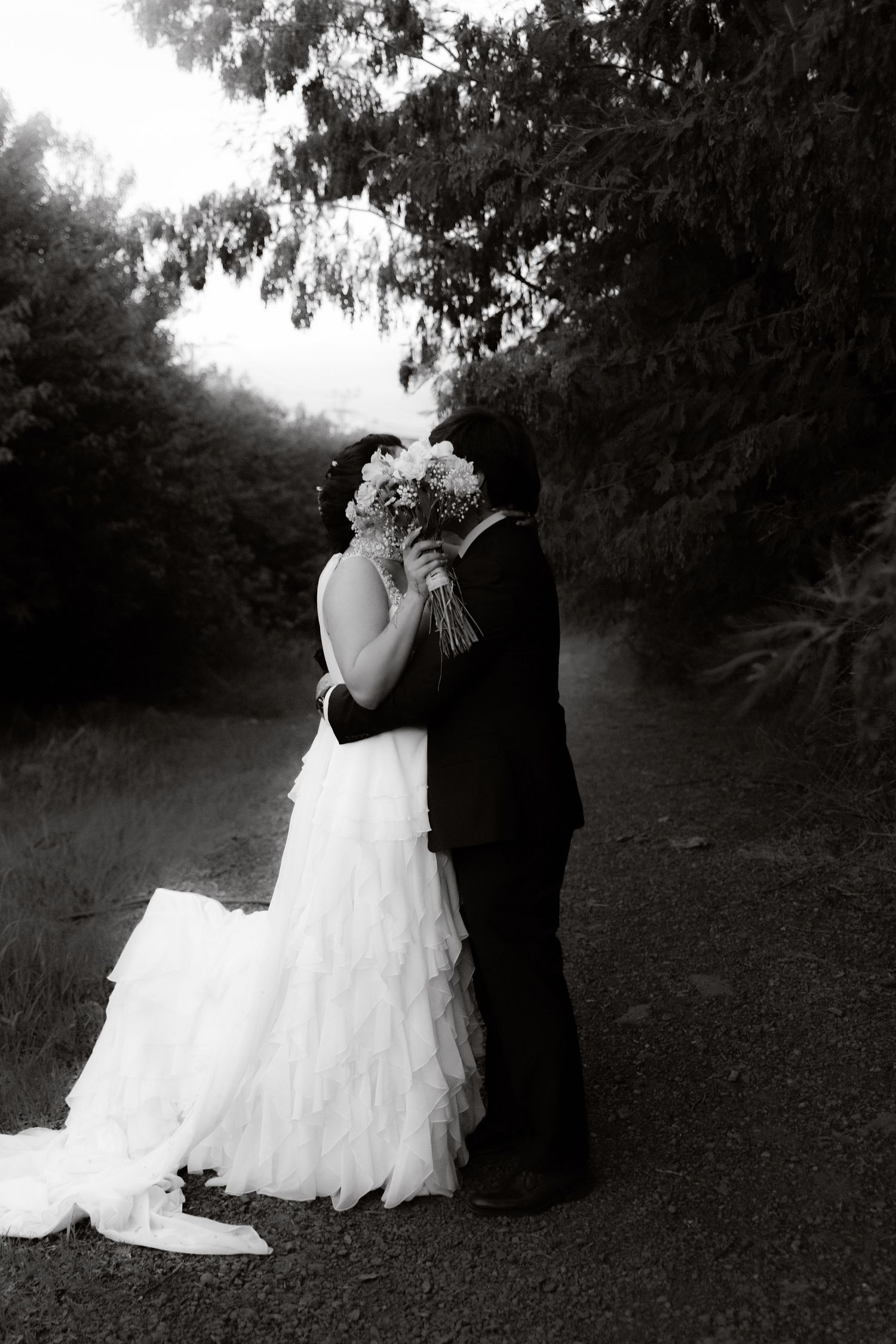 Black and white wedding photo of couple kissing while bouquet covers their faces outdoors.