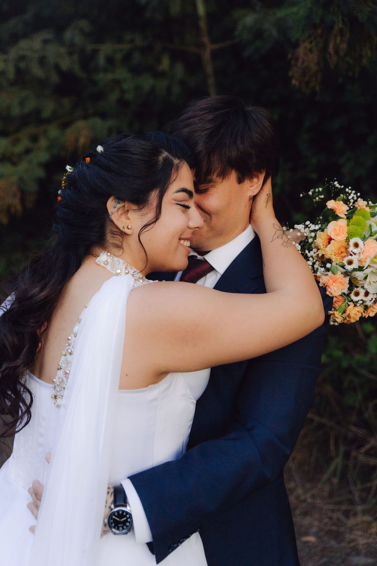 Bride and groom smiling with foreheads touching, bride in lace wedding dress holding peach floral bouquet.