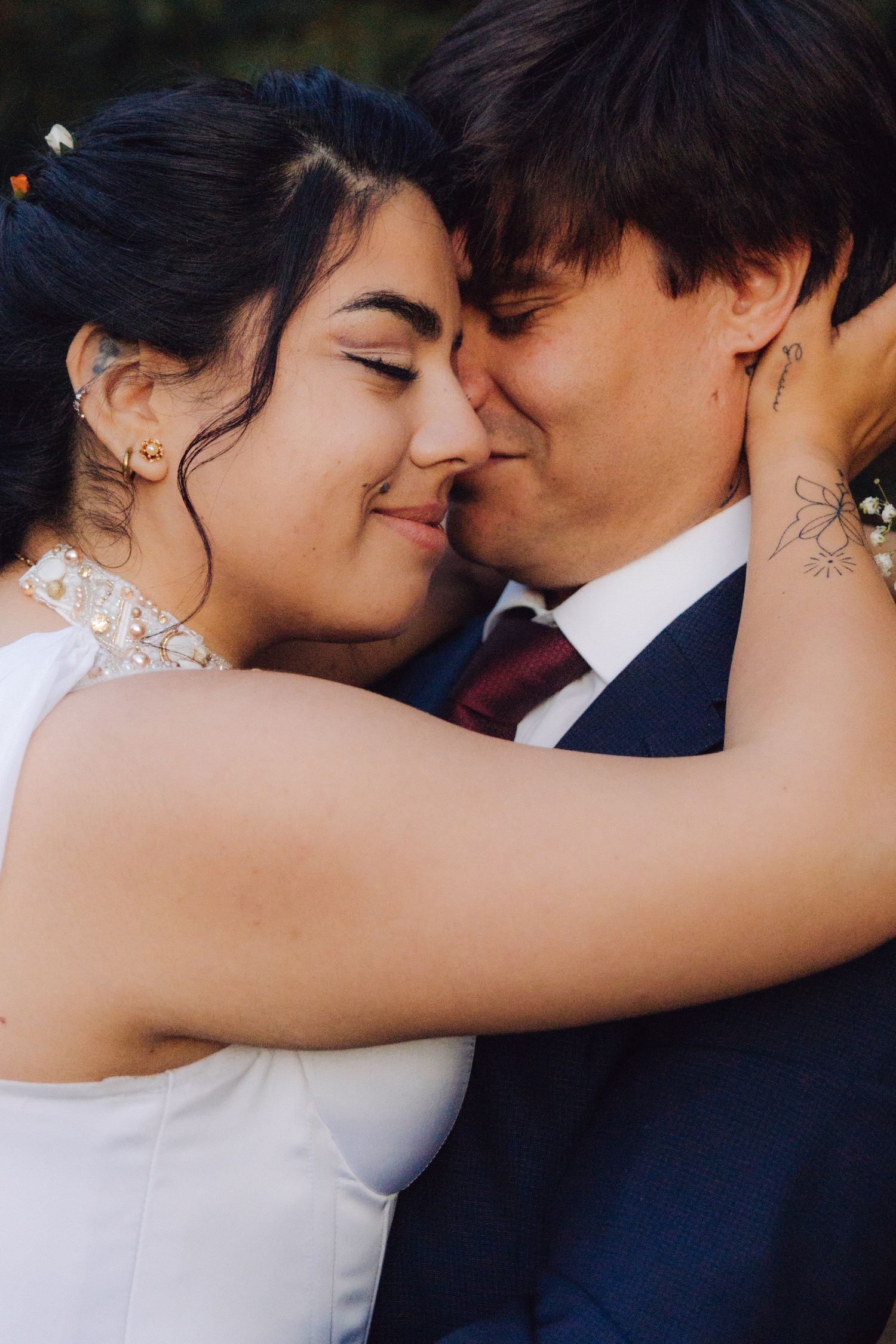 Bride and groom sharing an intimate moment, touching foreheads and smiling, bride in white dress with pearl details.