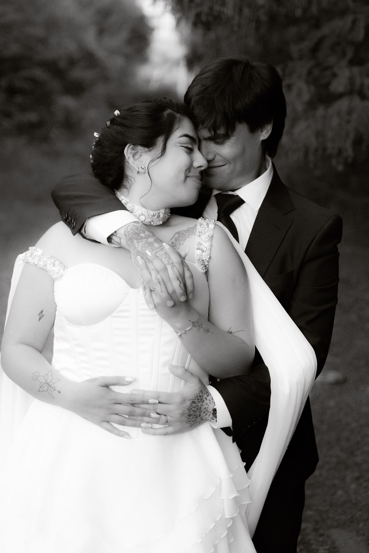 Black and white photo of a bride and groom embracing tenderly outdoors on their wedding day.