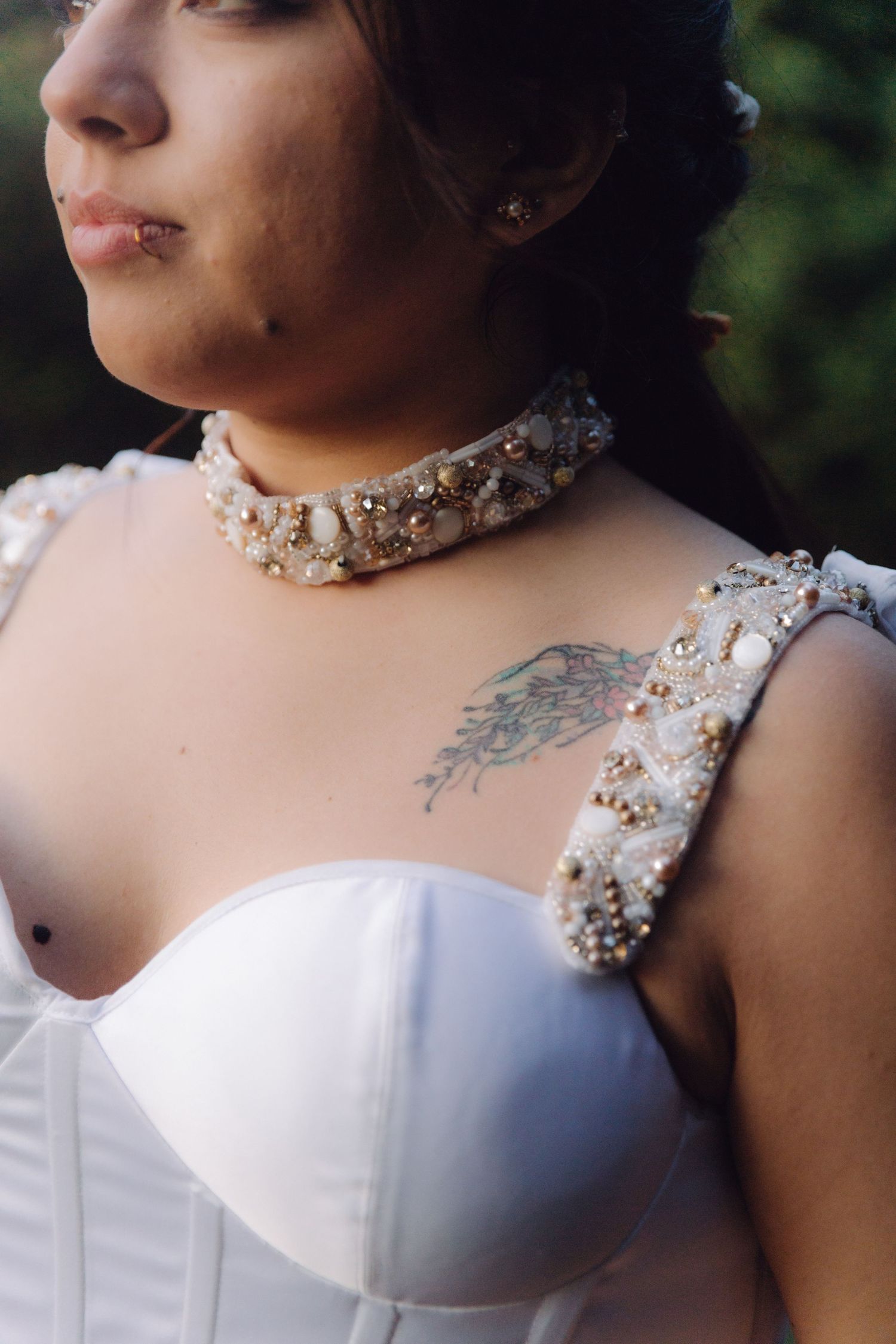 Close-up of bride in white wedding dress with pearl choker necklace and shoulder tattoo.