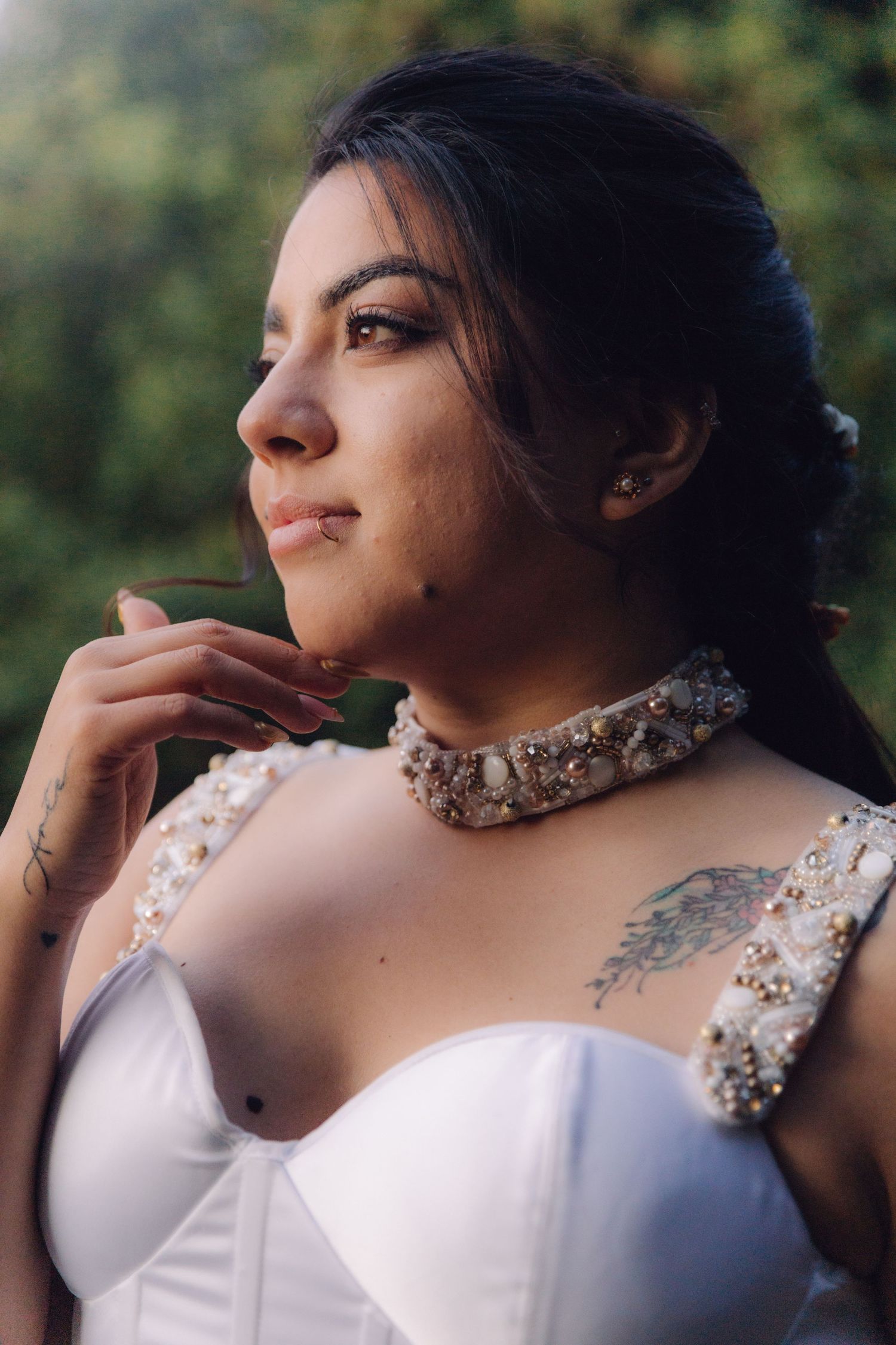 Beautiful bride in white wedding gown with pearl choker necklace gazing thoughtfully outdoors.