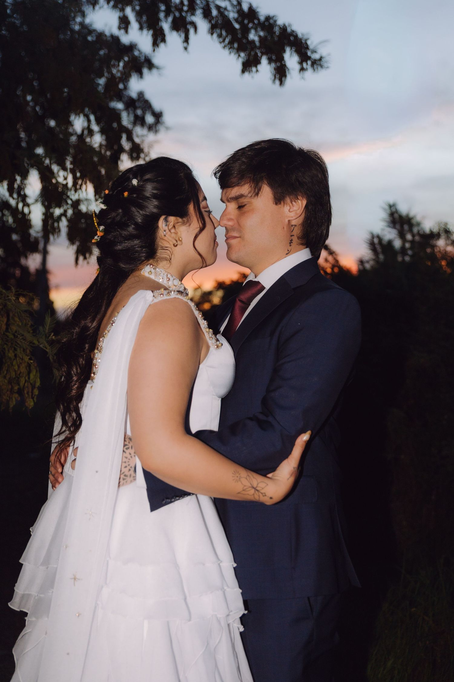Bride and groom sharing a romantic moment at sunset, dressed in wedding attire outdoors.