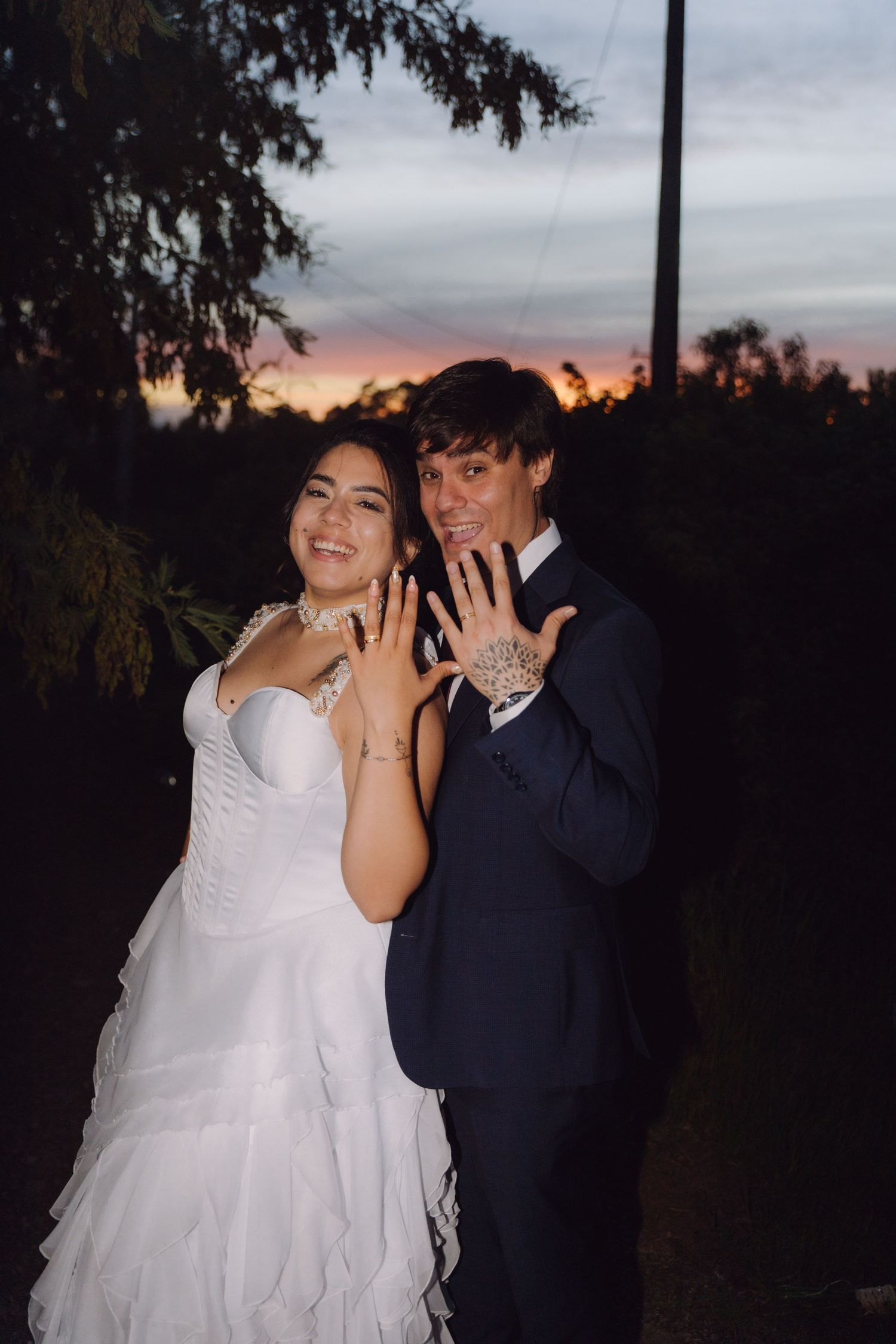 Joyful bride and groom showing wedding rings at sunset during outdoor wedding photography session.