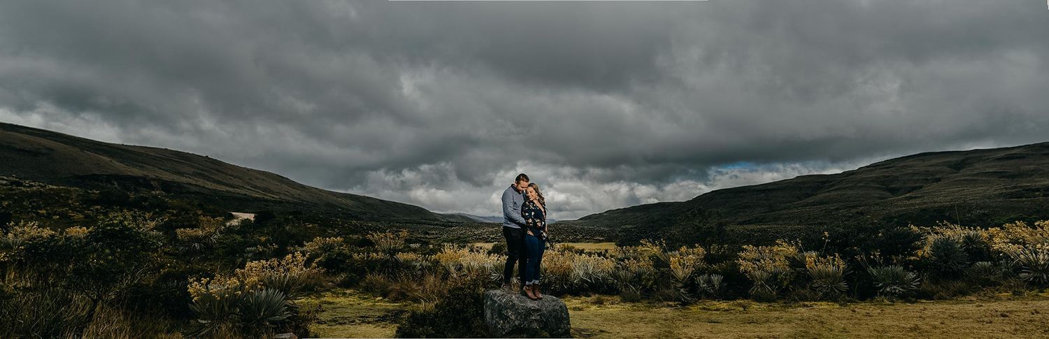 Couple embracing on a rock in a dramatic highland landscape under stormy skies.