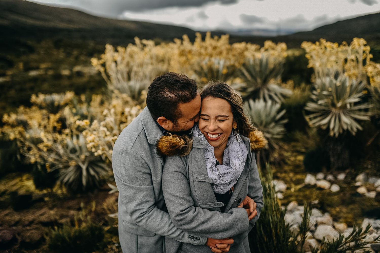 Couple embracing and laughing in a mountainous landscape with frailejones plants in the background.