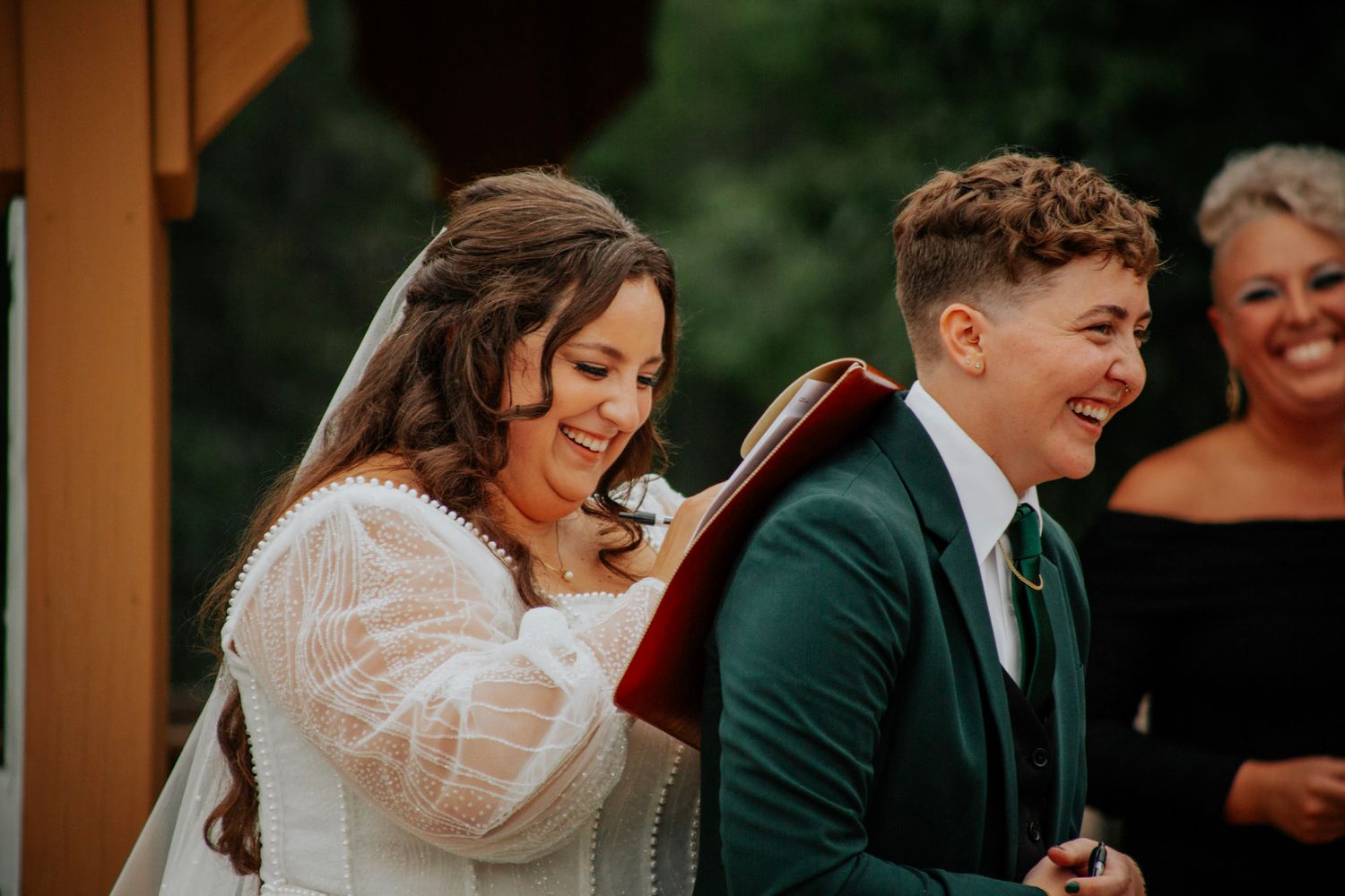 Bride and groom laugh joyfully during wedding ceremony at an outdoor woodland venue.