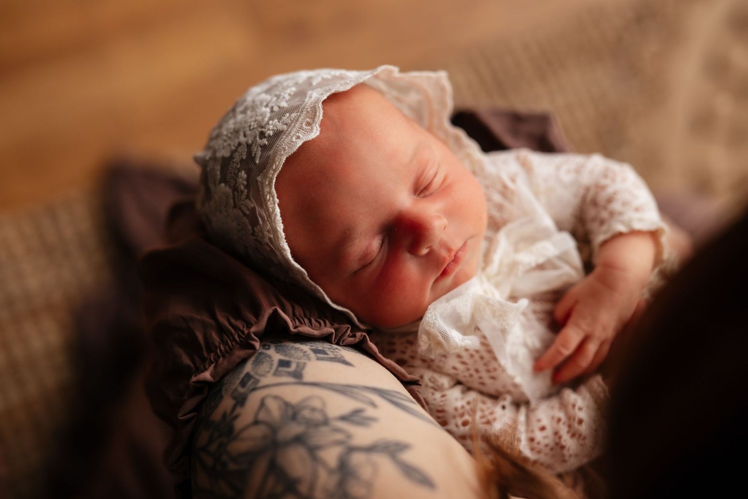 Sleeping newborn baby wearing a delicate lace bonnet, cradled in loving arms during a newborn photography session.