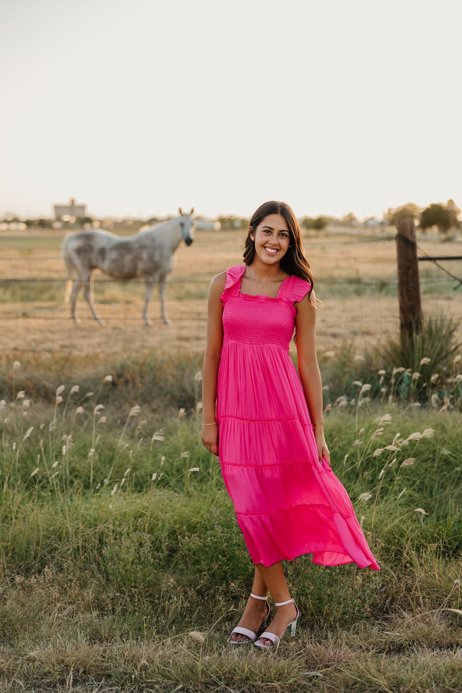 Senior girl in pink dress posing for photos in front of field and horses in Tulia, Texas