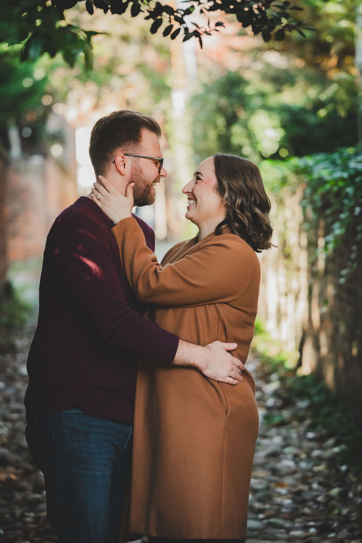 Couple facing each other and smiling in a sunlit ivy-covered alleyway during their engagement portraits
