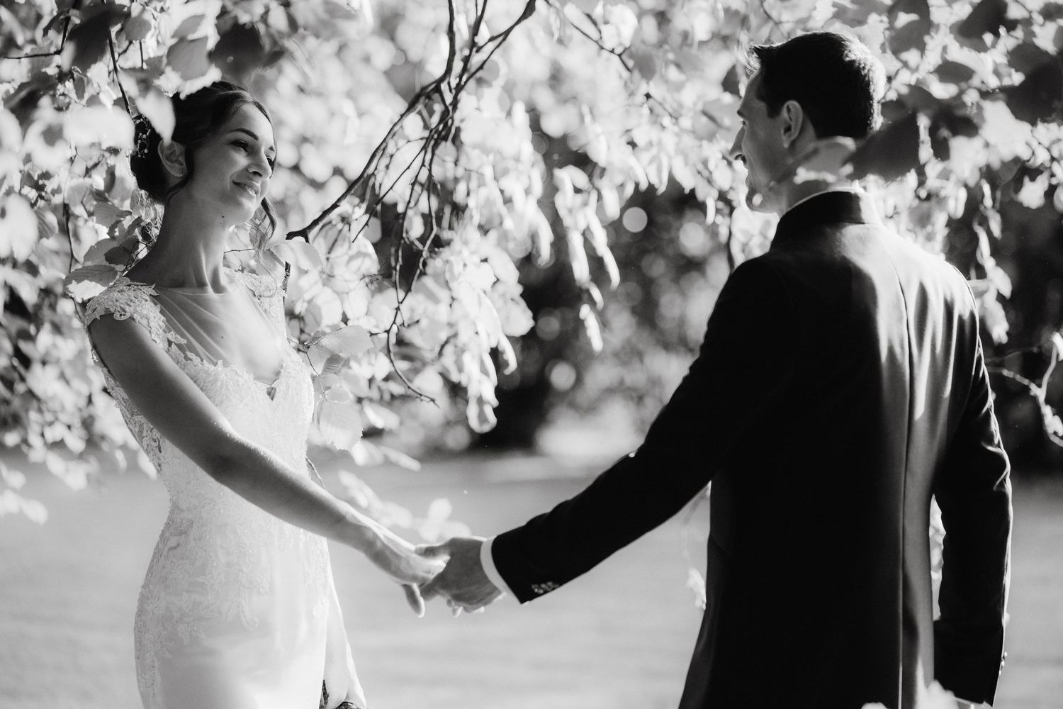 Black and white wedding photo of bride and groom holding hands under blooming cherry blossom tree.
