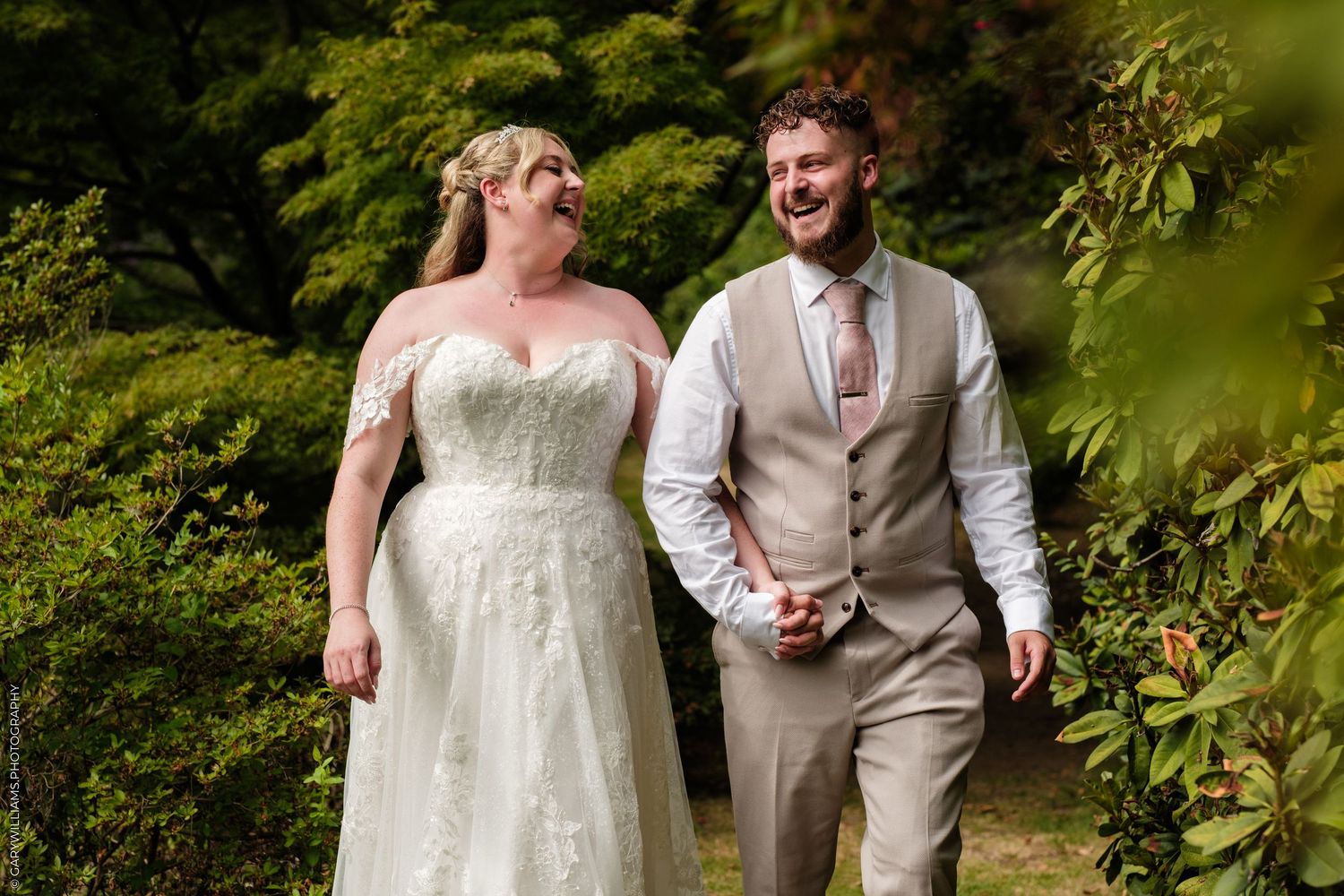 A joyful bride and groom walk hand in hand through a lush green garden on their wedding day.