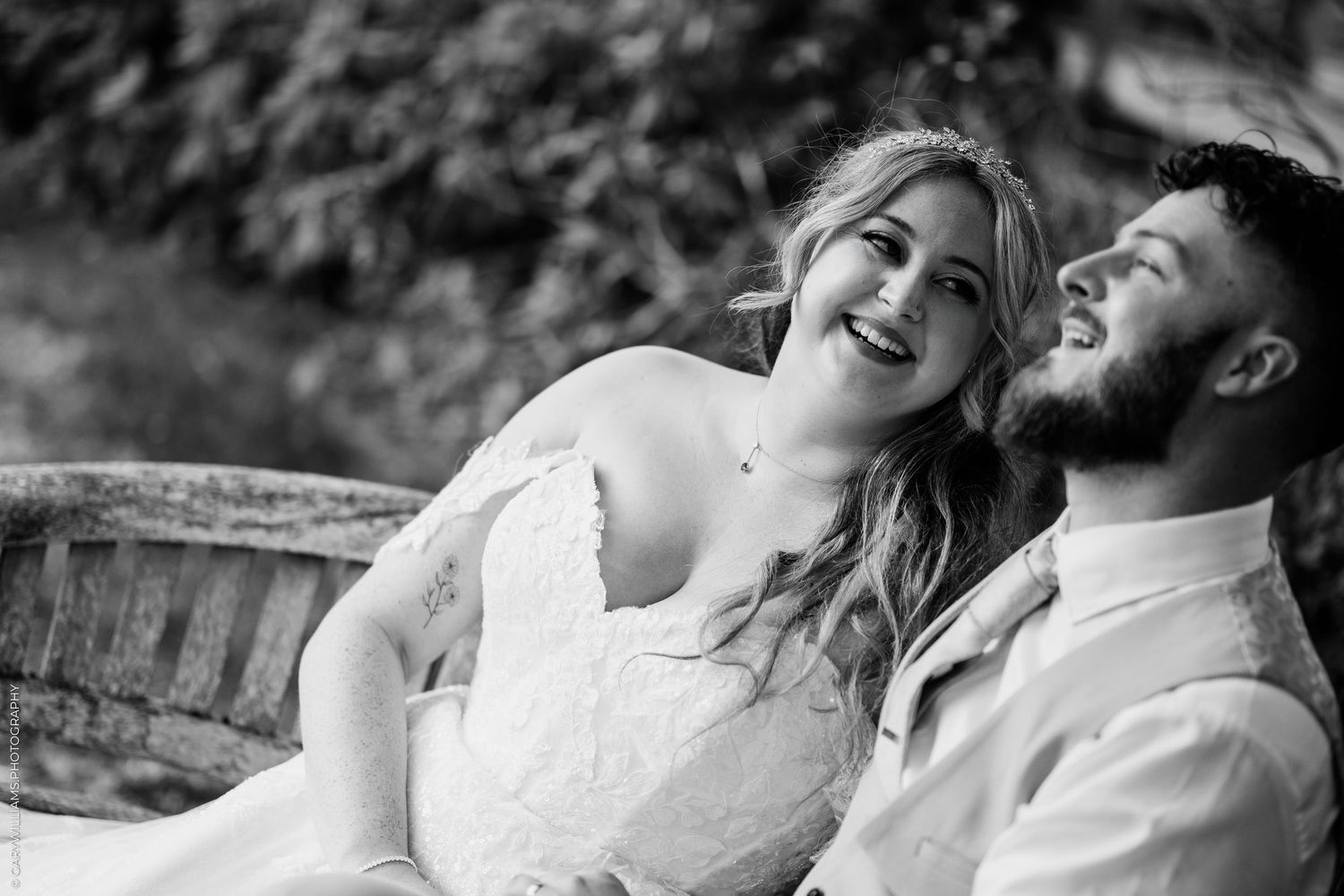 Black and white photo of a smiling bride and groom laughing together outdoors on their wedding day.
