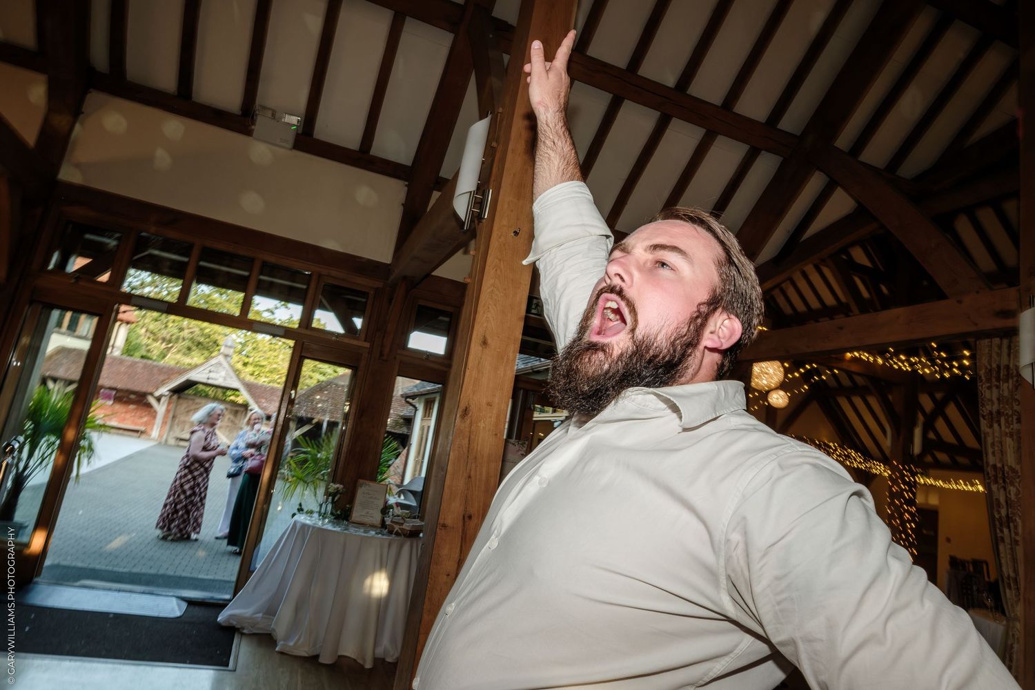 Excited man in white shirt reaching up at a rustic barn wedding reception venue.