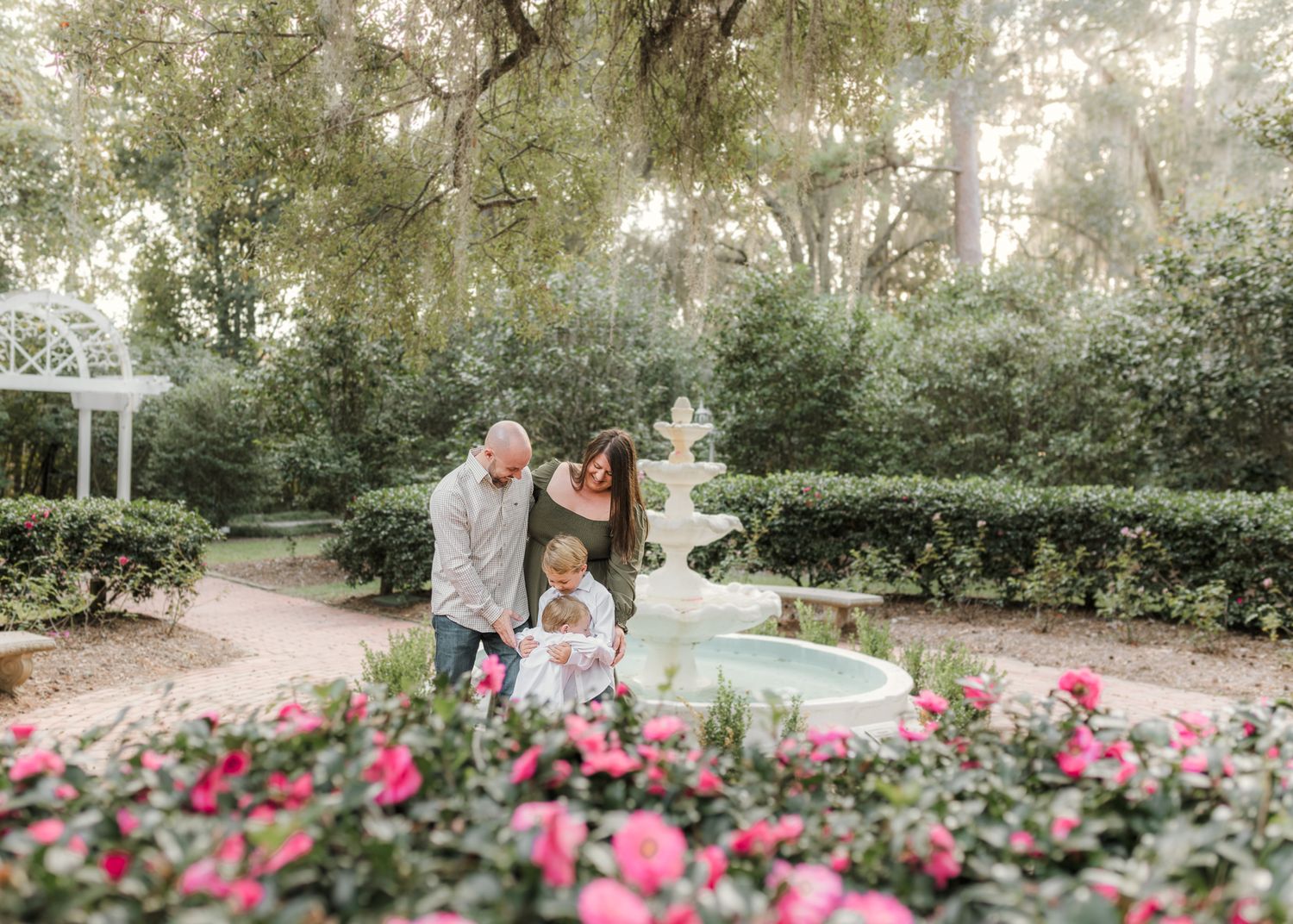 Couple sharing a romantic moment in a golden sunlit field with rose bushes and trees in the background.
