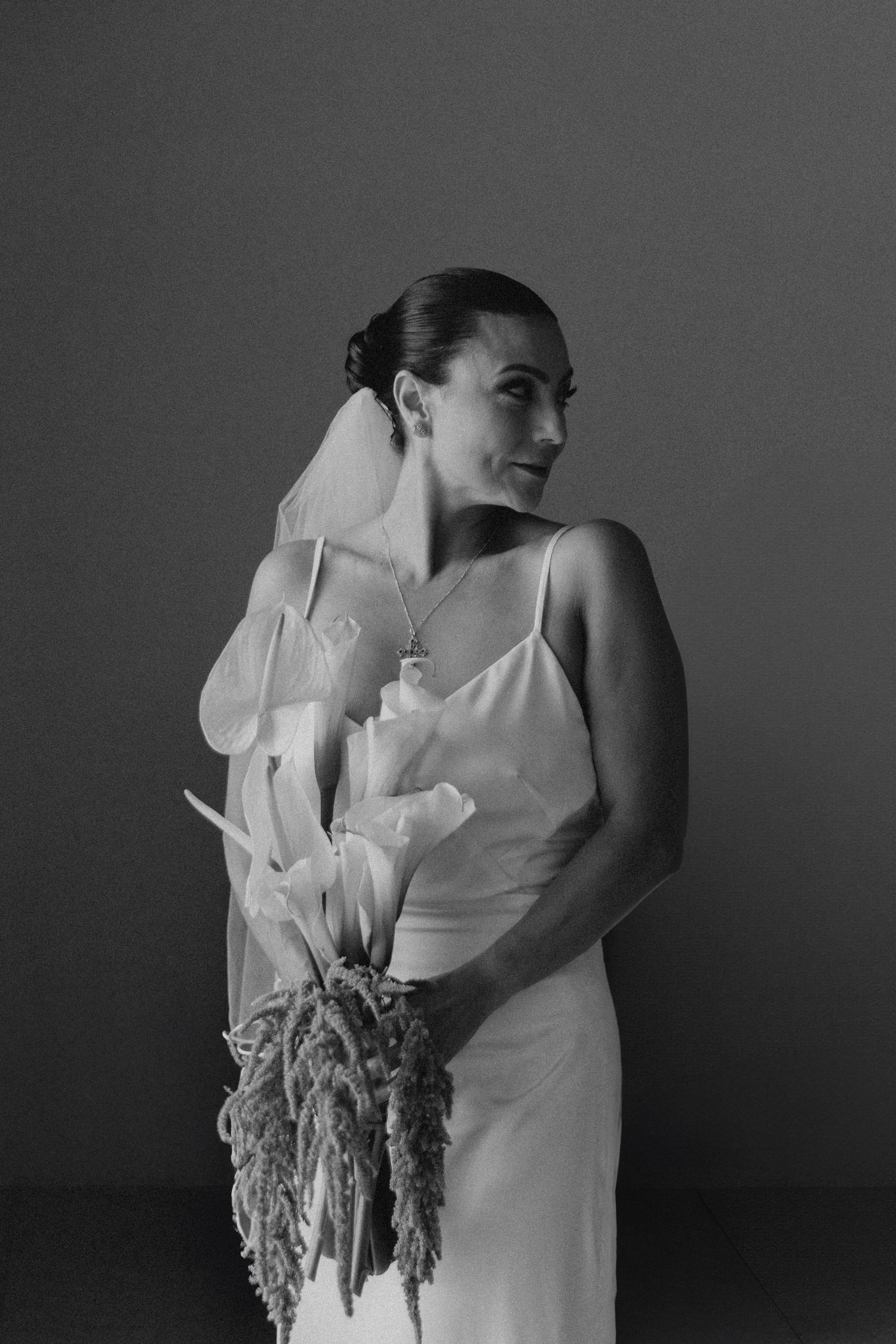 A bride smiles behind her colorful bouquet featuring pink and coral flowers with greenery and a flowing white veil.