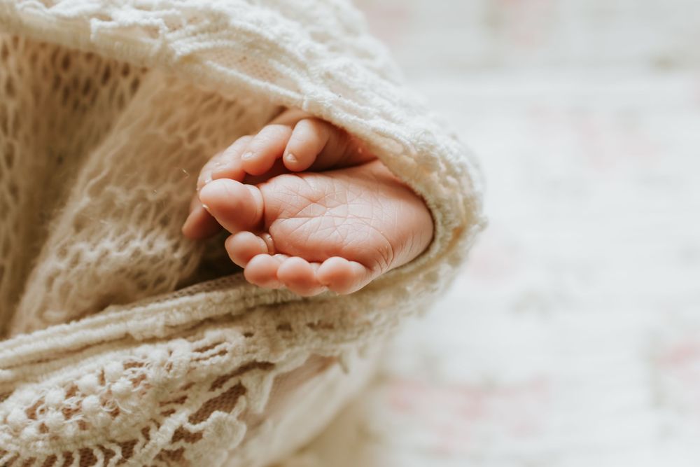 Close-up of a newborn baby's tiny hand peeking out from a soft cream knit blanket.
