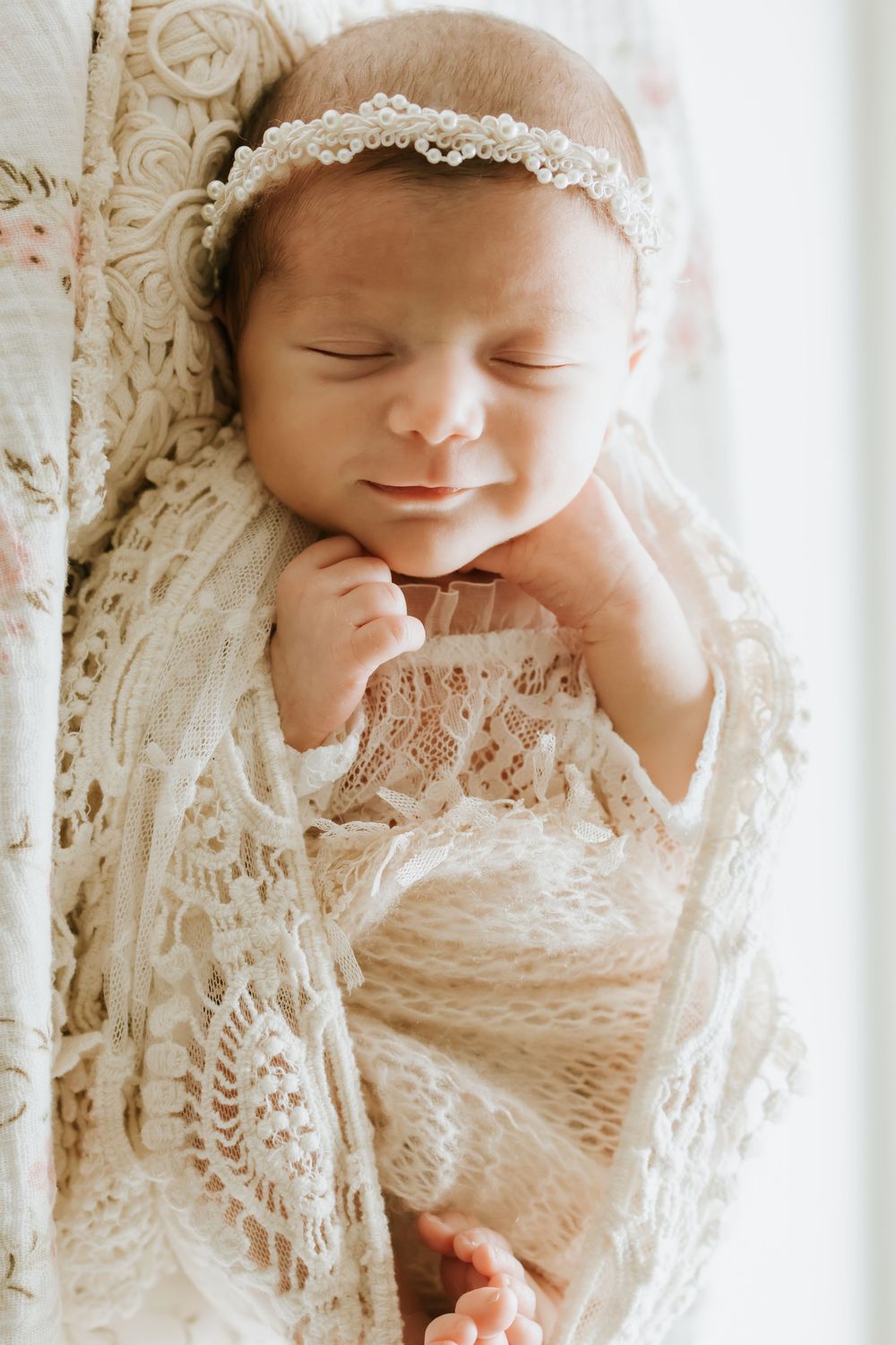 Sleeping newborn baby wrapped in cream lace swaddle wearing a delicate white floral headband.