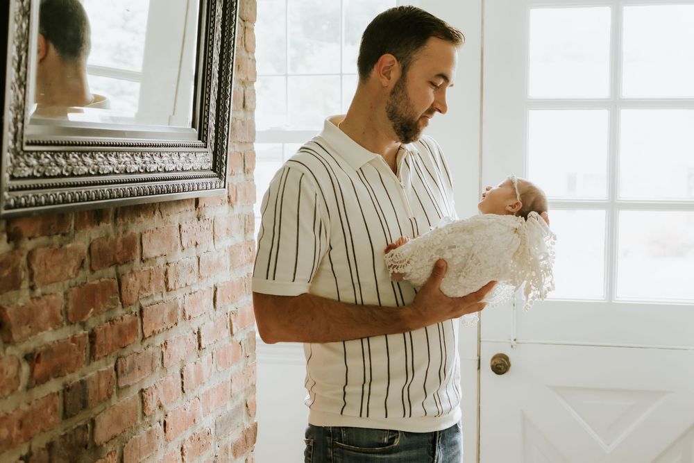 A father tenderly holds his newborn baby in a bright home entryway with exposed brick wall.