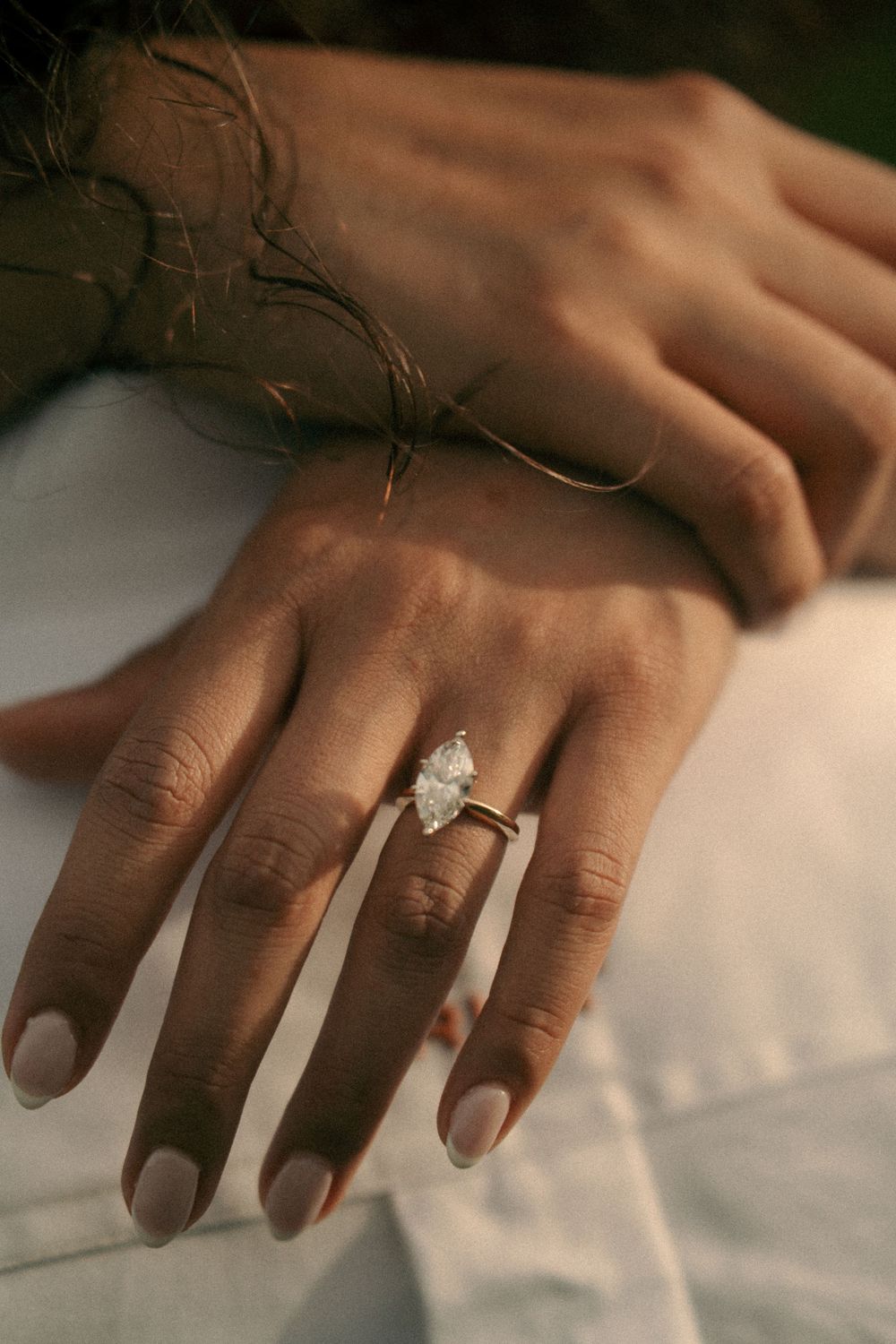 Close-up of a woman's hand wearing a marquise diamond solitaire engagement ring in gold, resting on a man's hand.