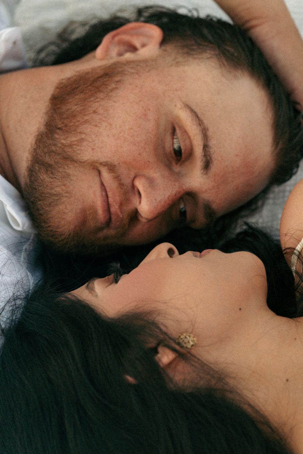 Close-up of romantic couple lying down, gazing at each other tenderly in an intimate portrait photo.