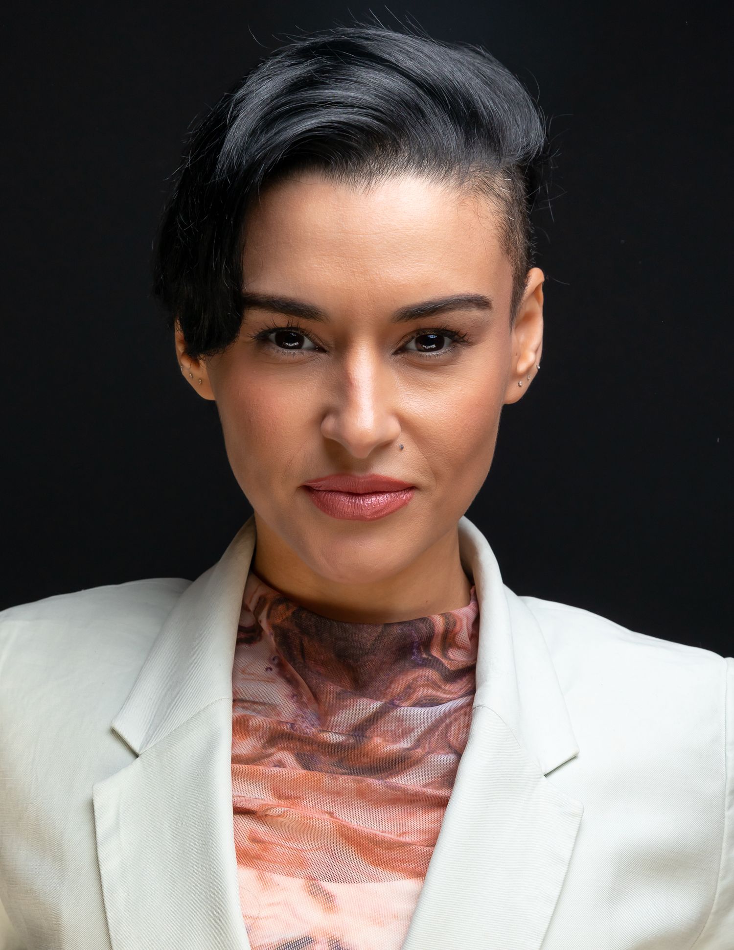 Professional headshot of a woman with short dark hair wearing a white blazer and colorful scarf.