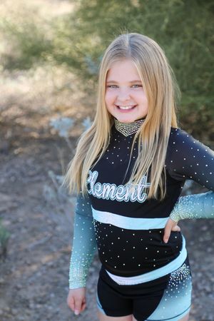 Smiling blonde girl with long straight hair poses with a hand on her hip in a black and teal Element cheer uniform.