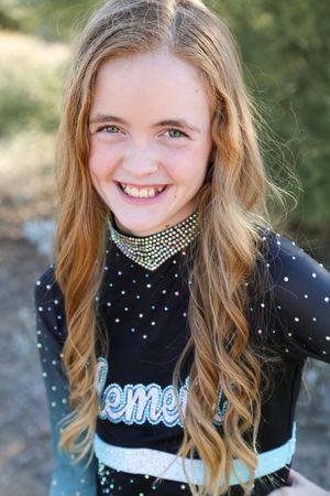 Close-up of a joyful girl with long wavy strawberry blonde hair wearing a black cheer top with a rhinestone collar.