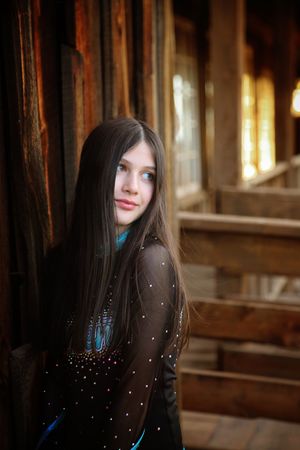 Girl with long dark hair glances over her shoulder in a sparkly black cheer top on a rustic wooden porch with warm glowing windows.